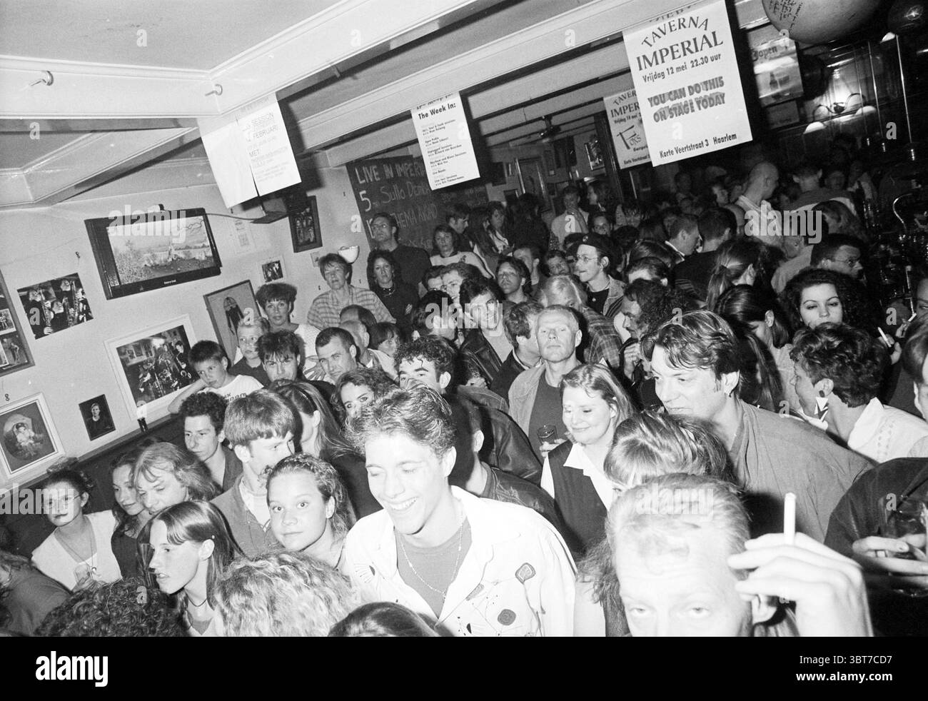 Themenabend „You CAN do this on Stage Today“ in Taverna Imperial Korte Veerstraat 3 Haarlem Korte Veerstraat Nederland, Whizgle News, Dutch Desk, Niederlande, 1950 - 2000 am 12.05.1995. Diese Themen sind in der Abbildung dargestellt. Die Szene strotzt vor Energie, während eine dichte Menschenmenge einen lebendigen Innenraum füllt, wahrscheinlich einen Pub oder eine Bar. Die Atmosphäre ist lebendig, mit einer Mischung aus Ausdrucksformen, die von Lachen bis zu tiefen Gesprächen reichen, was auf ein Gefühl von Kameradschaft unter den Teilnehmern hinweist. Die Menge besteht aus einer vielfältigen Gruppe von Menschen, mit verschiedenen Frisuren und Kleidungsstilen von lässig bis etwas mehr Stockfoto