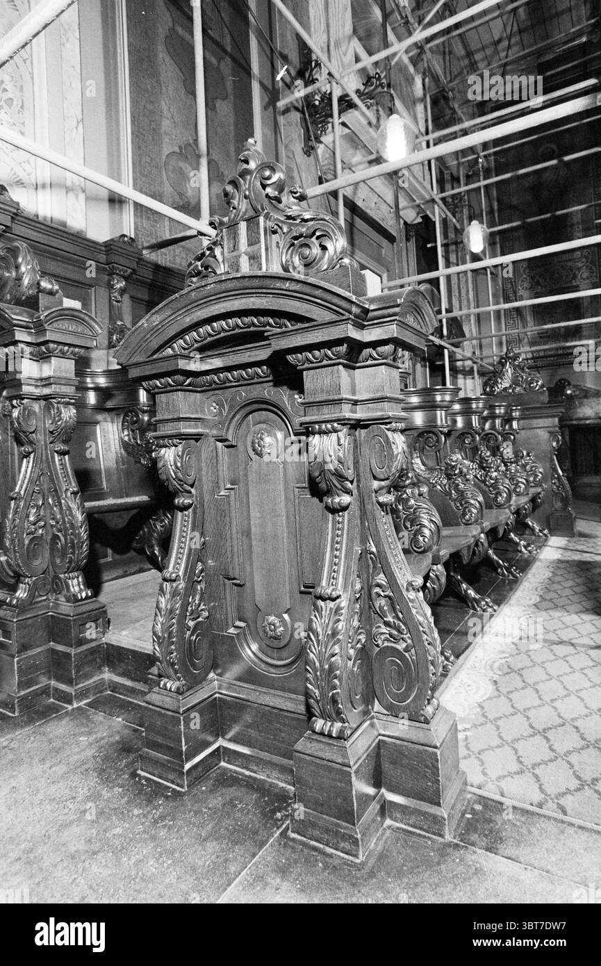 Sonstiges. Joseph Church, Whizgle News, Dutch Desk, Niederlande, 1950 - 2000 am 03-12-1992. Das Bild enthält diese Themen. Die Szene zeigt einen Innenraum mit opulenten architektonischen Details und reichen Holzelementen. Im Vordergrund stehen aufwändig geschnitzte Holzbänke, deren dunkle, glänzende Oberflächen die Handwerkskunst des Designs betonen. Jede Bank ist mit kunstvollen Motiven wie Blumenmustern und rollenden Reben versehen, die auf eine historische oder zeremonielle Bedeutung hinweisen. Hinter den Bänken zeigt sich ein großes Inneres, möglicherweise eine Kathedrale Stockfoto