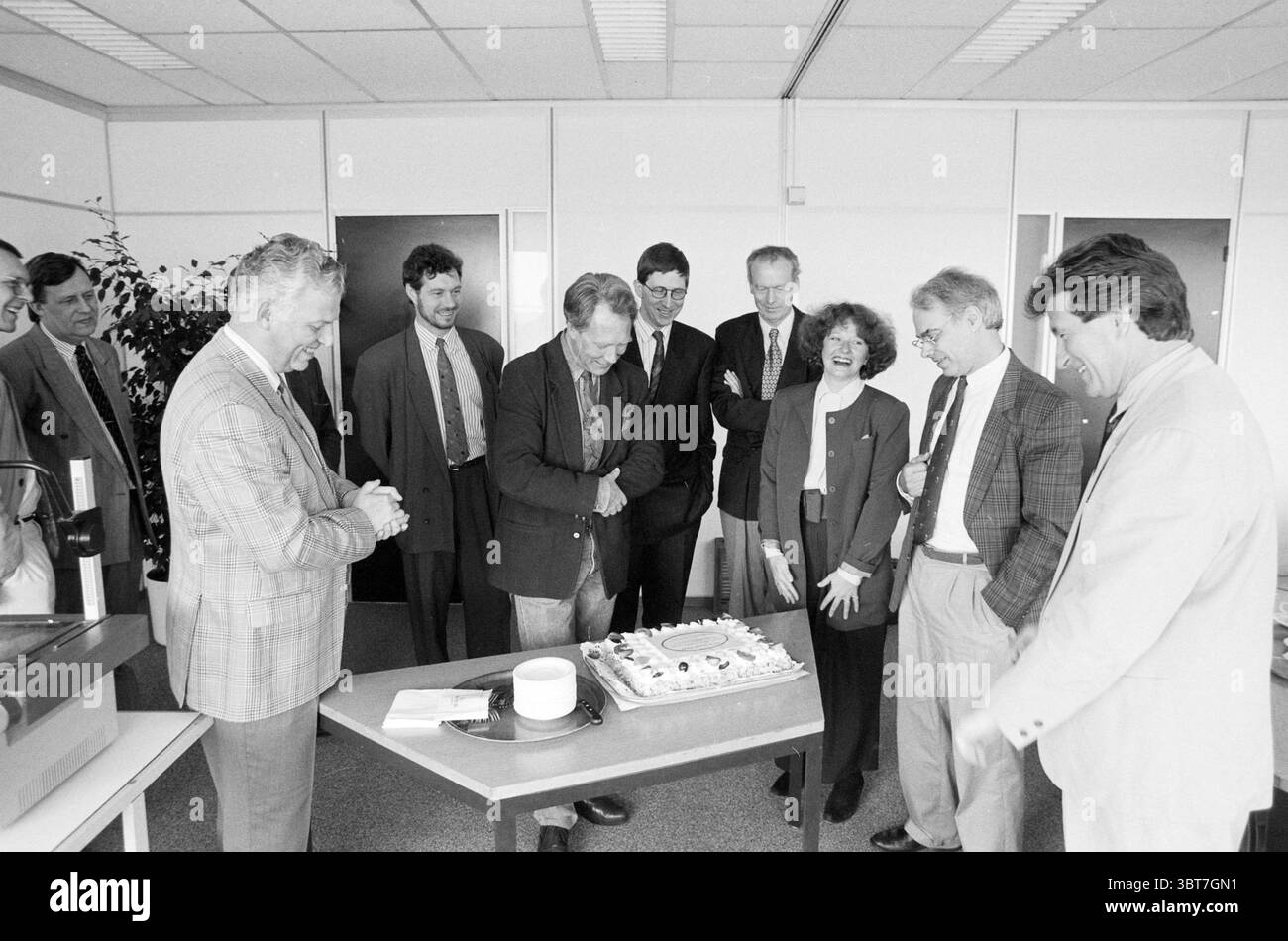 NRM Meeting Waarderpolder Haarlem the Netherlands, Whizgle News, Dutch Desk, Niederlande, 1950 - 2000 am 24-03-1991. Diese Themen werden in der Abbildung angezeigt. In einer geräumigen, modernen Büroumgebung versammelt sich eine Gruppe von Einzelpersonen um einen großen, dekorierten Kuchen auf einem Tisch. Das Zimmer hat eine saubere, professionelle Ästhetik, die an den neutralen Wänden und den eleganten Möbeln zu erkennen ist. Die Teilnehmer zeigen eine Mischung aus formeller und halbformaler Kleidung, die auf einen feierlichen Anlass hindeutet, wahrscheinlich zu Ehren eines Kollegen oder einen wichtigen Meilenstein. Die Stimmung ist warm und fröhlich. Mehrere Leute lächeln Stockfoto