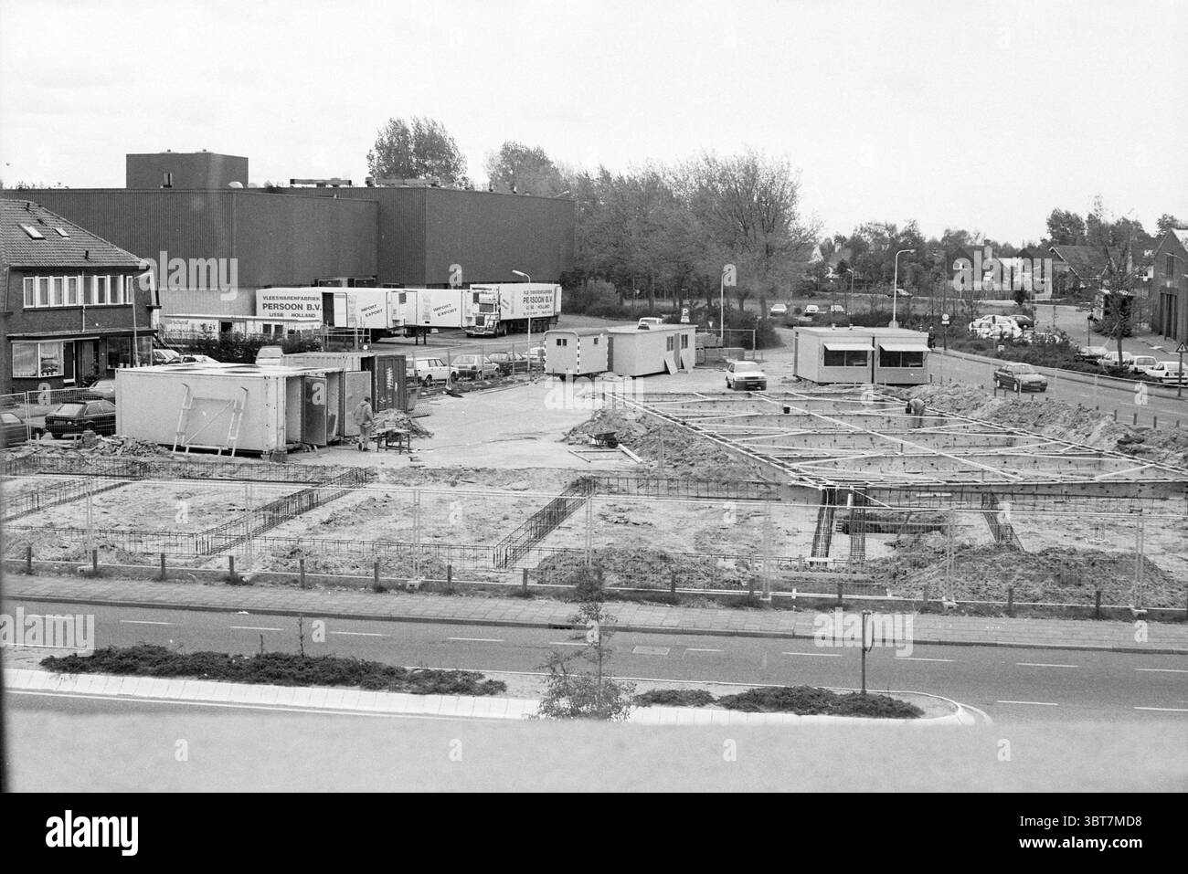 Bauen Sie Wohnungen in Bloemendaal Bloemendaal, Whizgle News, Dutch Desk, Niederlande, 1950 - 2000 am 14-05-1991. Die Abbildung zeigt diese Themen. Die Szene zeigt eine Baustelle, die sich in der frühen Entwicklungsphase befindet. Der Boden ist größtenteils unfruchtbar, überall verstreut sind Schutt- und Schutthaufen. Es werden Rahmenkonstruktionen, möglicherweise für ein Fundament, eingerichtet, die zeigen, wo Gebäude schließlich Gestalt annehmen werden. Im Vordergrund verläuft parallel zum Gelände eine gepflasterte Straße, die von einem kleinen Grünstreifen aus niedrigen Sträuchern und einigen Grasflecken begrenzt wird. Zwei Disti Stockfoto