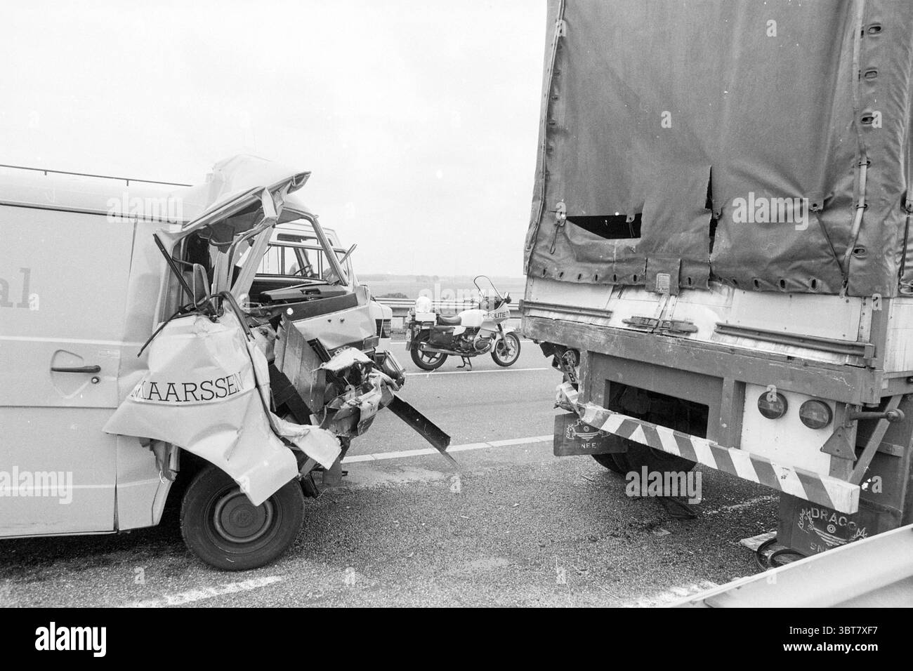 Der Van ist auf der Autobahn in den Truck gestürzt. Verkehrsunfall, Whizgle News, Dutch Desk, Niederlande, 1950 - 2000 am 09-1987. Dies sind die Elemente im Bild. Die Szene zeigt einen Straßenunfall, bei dem ein kleiner Lieferwagen mit dem Heck eines großen Lkws kollidiert. Der Van, der sich durch seine zerknitterte Front und die verbeulten Seiten auszeichnet, weist erhebliche Schäden auf, was auf einen starken Aufprall hindeutet. Seine Türen sind offen, und es gibt sichtbare zersplitterte Glasstücke, die verstreut sind. Der aufragende und imposante Lkw weist ein klaffendes Loch im Heck auf, was auf die Intensität des Aufpralls hindeutet. Seine Oberfläche ist verdunkelt, Witz Stockfoto