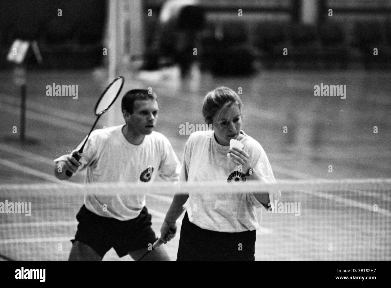 Badminton Let it be Champion Haarlem the Netherlands, Whizgle News, Dutch Desk, Niederlande, 1950 - 2000 am 20.01.1996. Diese Themen sind in der Abbildung dargestellt. In einem geräumigen Indoor-Gymnasium spielen zwei Personen Badminton. Die Einrichtung hat einen polierten Holzboden, der die Deckenleuchten reflektiert und einen warmen Glanz verleiht. Die Wände sind mit gedämpften Farben ausgekleidet, was die Sauberkeit und Einfachheit der Umgebung verbessert. Ein Spieler, ein Mann, ist links positioniert, leicht gehockt mit einem fokussierten Ausdruck. Er trägt ein schlichtes weißes T-Shirt und dunkle Shorts. Sein Griff auf den Badm Stockfoto