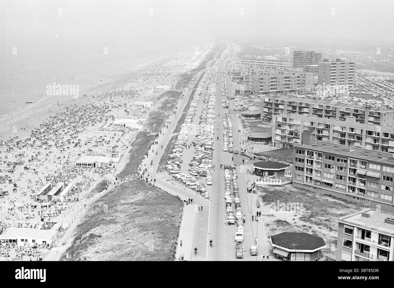 By Zandvoort By Zandvoort, Whizgle News, Dutch Desk, Niederlande, 1950 - 2000 am 07-06-1965. Das Bild enthält diese Themen. Die Szene fängt ein lebhaftes Küstengebiet ein. Auf der linken Seite erstreckt sich ein Sandstrand entlang der Küste, der von zahlreichen Sonnenanbetern, leuchtenden Sonnenschirmen und farbenfrohen Handtüchern gesäumt ist. Die Menschen genießen ihre Zeit, einige faulenzen, während andere aktiv Strandspiele spielen, schwimmen oder am Ufer entlang spazieren gehen. Im Vordergrund verläuft parallel zum Strand eine breite, gepflasterte Straße, gesäumt von einer Mischung aus geparkten Autos in verschiedenen Farbtönen, von klassischen Weißtönen Stockfoto