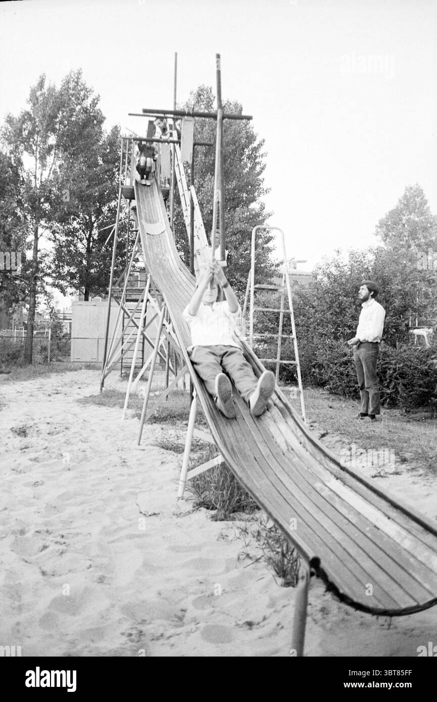 Partyspielplatz Floragaarde Festival Festivitäten und Manifestationen Spielplätze und Spielplätze, Whizgle News, Dutch Desk, Niederlande, 1950 - 2000 am 17-06-1972. Die Abbildung zeigt diese Themen. Die Szene zeigt eine lebhafte Spielplatzumgebung, die von einer großen Holzrutsche dominiert wird, die sich anmutig nach unten dreht. Die Rutsche steht vor einem Hintergrund von hoch aufragenden Bäumen, deren Blätter eine Mischung aus lebhaftem Grün und gelben Anklängen bilden, die auf eine Spätsommer- oder Frühherbstatmosphäre hinweisen. Im Vordergrund gleitet ein Kind in hellem Hemd und Shorts freudig über die Rutsche, die Arme sind erregt hoch. Stockfoto Partyspielplatz Floragaarde Festival Festivitäten und Manifestationen Spielplätze und Spielplätze, Whizgle News, Dutch Desk, Niederlande, 1950 - 2000 am 17-06-1972. Die Abbildung zeigt diese Themen. Die Szene zeigt eine lebhafte Spielplatzumgebung, die von einer großen Holzrutsche dominiert wird, die sich anmutig nach unten dreht. Die Rutsche steht vor einem Hintergrund von hoch aufragenden Bäumen, deren Blätter eine Mischung aus lebhaftem Grün und gelben Anklängen bilden, die auf eine Spätsommer- oder Frühherbstatmosphäre hinweisen. Im Vordergrund gleitet ein Kind in hellem Hemd und Shorts freudig über die Rutsche, die Arme sind erregt hoch. Stockfoto