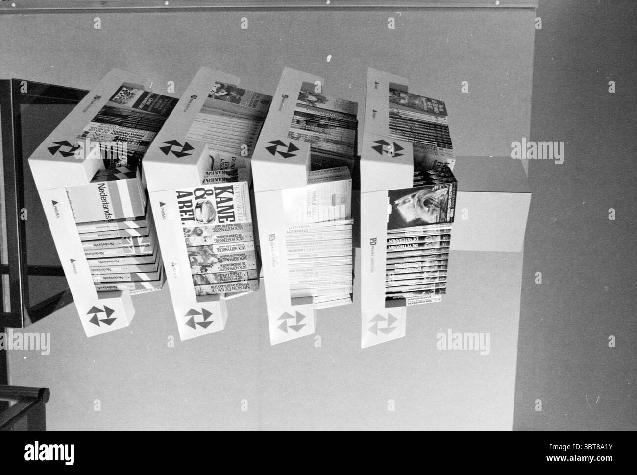Buchstand Spectrum de Meern Spectrum, Whizgle News, Dutch Desk, Niederlande, 1950 - 2000 am 18-08-1982. Das Bild enthält diese Themen. In einem minimalistischen Ambiente bietet ein einzigartiges Display verschiedene Magazine und sorgt so für einen beeindruckenden visuellen Effekt. Die Magazine sind in einem kaskadierenden Muster angeordnet, wobei einige nach vorne zeigen, während andere seitlich gedreht werden und lebendige Cover zeigen. Das Farbschema besteht hauptsächlich aus Schwarz-weiß und unterstreicht den starken Kontrast der Zeitschriften vor dem helleren Hintergrund. Die Anzeigeeinheit selbst ist mit klaren Linien gestaltet und bietet eine moderne Ästhetik Stockfoto