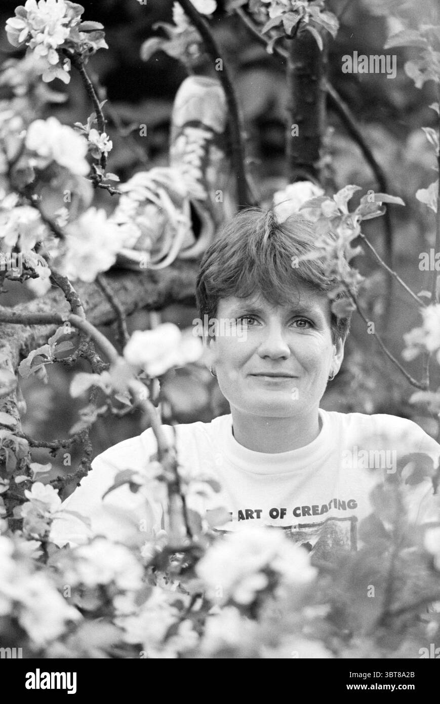 Marianne van der Linde Marathon, Whizgle News, Dutch Desk, Niederlande, 1950 - 2000 am 10-05-1994. Das Bild enthält diese Themen. In der Szene wird eine Person inmitten blühender Blumen positioniert und bildet einen natürlichen Rahmen um ihr Gesicht. Die Person hat eine kurze Frisur und einen sanften Ausdruck, der den Betrachter mit einem Gefühl von Ruhe und Gelassenheit direkt anblickt. Sie sind in einem hellen Oberteil gekleidet, das einen subtilen Kontrast zu den zarten Blüten um sie herum bildet. Die Blüten, weiß mit rosa Anklängen, sind üppig und üppig, füllen den Vordergrund und schaffen eine weiche, traumhafte Atmosphäre. Stockfoto