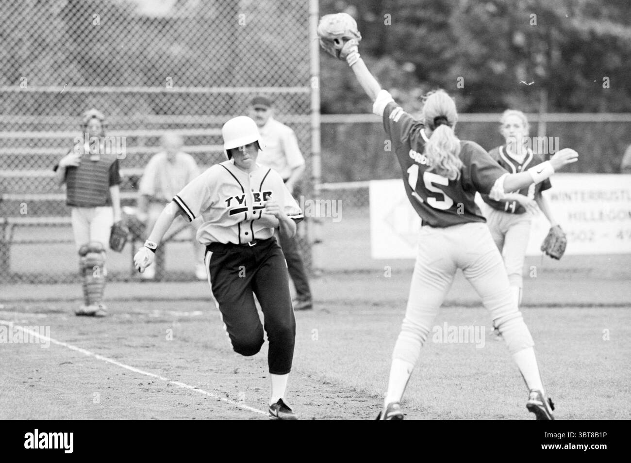 Softball: TYBB-DSC 74, Whizgle News, Dutch Desk, Niederlande, 1950 - 2000 am 07-06-1997. Diese Themen werden in der Abbildung angezeigt. In einer dynamischen Sportszene sind zwei Spieler in einem angespannten Moment auf dem Spielfeld aktiv. Ein Athlet trägt ein graues Trikot mit dem Aufdruck „TYERS“ auf der Vorderseite, trägt einen weißen Helm und rennt auf eine Basis zu, um Entschlossenheit und Mühe zu zeigen. Der andere Spieler, der in einem knallroten Trikot mit der Zahl „15“ gekleidet ist, ist verteidigend positioniert, um einen Wurf zu erhalten. Ihr Ausdruck zeigt Konzentration und Bereitschaft, während sie sich auf ein Spiel vorbereitet. Im Hintergrund additio Stockfoto