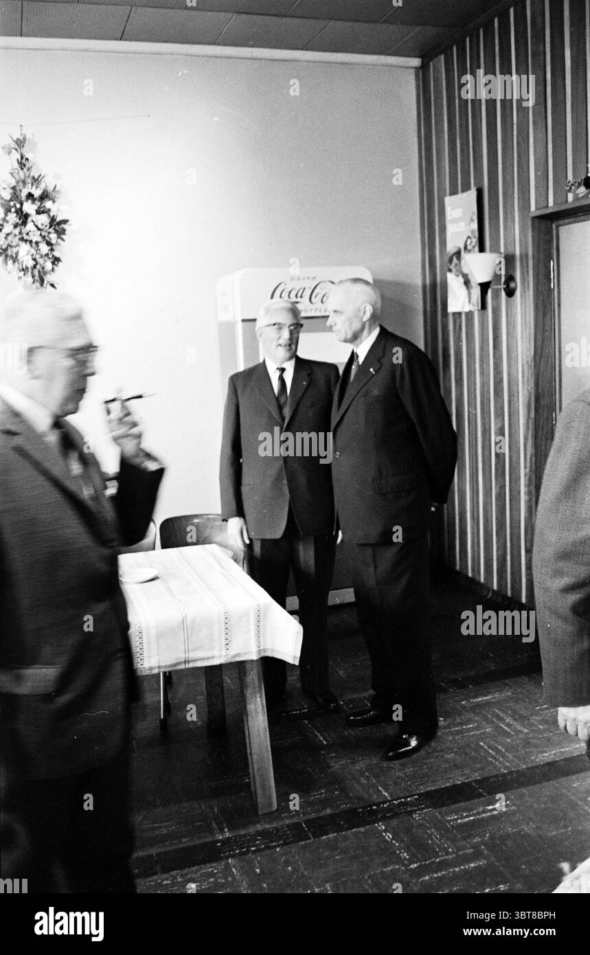 1. Stapel der neuen Fabrik. Größe Haarlem Paul Krugerkade The Netherlands, Whizgle News, Dutch Desk, Niederlande, 1950 - 2000 am 22-03-1961. Dies sind die Themen im Bild. In einem gut beleuchteten Innenraum mit Holzvertäfelung stehen zwei formale Figuren dicht beieinander und führen Gespräche. Beide sind in dunklen Anzügen und Krawatten gekleidet, was einen Hauch von Professionalität vermittelt. Ein Individuum ist etwas größer, mit weißem Haar, während das andere sich durch seinen Glatzkopf auszeichnet. Beide Ausdrücke vermitteln einen Moment aufmerksamen Dialogs. Im Hintergrund ein Coca-Cola-Automaten Stockfoto