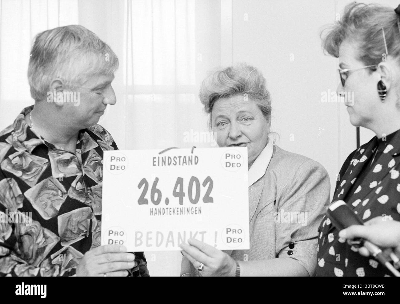 Unterschriftenübergabe durch das Deo an Bürgermeister Schultz Haarlem, Niederlande, Whizgle News, Dutch Desk, Niederlande, 1950 - 2000 am 24.05.1993. Dies sind die Themen im Bild. In der Szene werden drei Individuen zusammen positioniert, deren Ausdruck eine Mischung von Emotionen vermittelt. Links steht ein Mann mittleren Alters, der ein gemustertes Hemd mit auffälligen Farben trägt, das durch seine Wirbel und Umrisse einen lebendigen Look schafft. Er hat helles Haar und sieht leicht zur Seite, was ein engagiertes Verhalten widerspiegelt. In der Mitte dominiert eine Frau mit ihrem voluminösen, gestylten Haar die Aufmerksamkeit Stockfoto