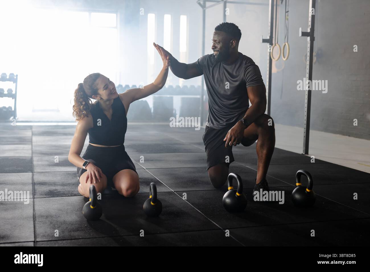 Verschiedene Trainingspartner heben Kettlebells im Fitnessstudio mit Fitness-Tracker unter Ringen Stockfoto