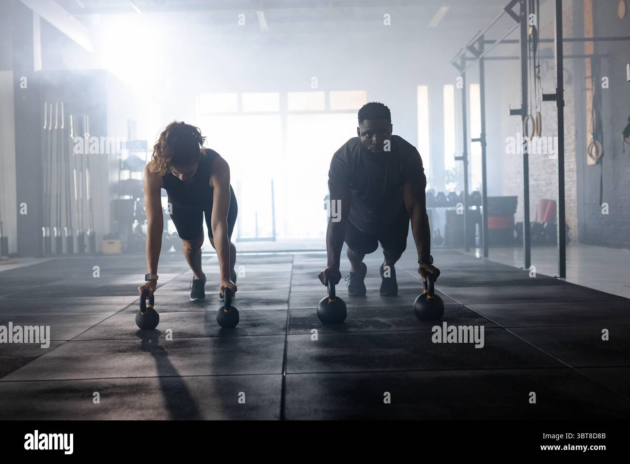 Verschiedene Workout-Partner halten Kettlebells und balancieren auf der Matte im Trainingsraum mit Rigs Stockfoto