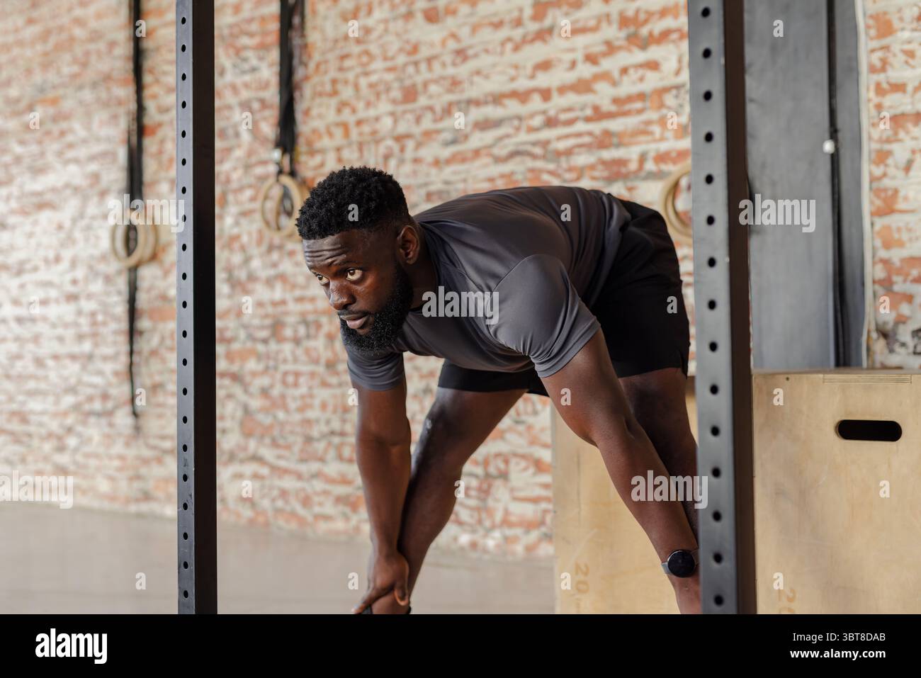 Afroamerikanischer Mann, der sich in einem CrossFit-Fitnessstudio mit Sportbekleidung auf einem Metallhocker stützt Stockfoto