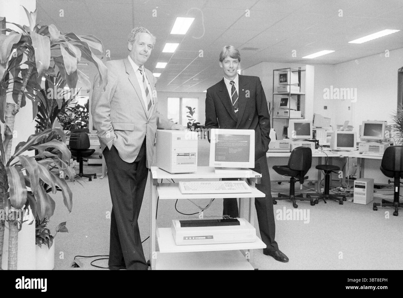 Mr. Compaan und Lobken K.N. Badhoevedorp Computer People Companies Badhoevedorp, Whizgle News, Dutch Desk, Niederlande, 1950 - 2000 auf 30-05-1989. Das Bild enthält diese Themen. Die Szene spielt in einer geräumigen Büroumgebung, die durch eine helle und offene Atmosphäre gekennzeichnet ist. Zu den vorherrschenden Farben gehören weiß- und Grautöne, die zu einem sauberen und professionellen Look beitragen. Im Vordergrund stehen zwei Männer neben einem Arbeitsplatz. Ein Mann trägt einen hellgrauen Anzug mit gemusterter Krawatte, der Autorität und Professionalität vermittelt. Er hat eine selbstbewusste Haltung, die Arme sind entspannt Stockfoto
