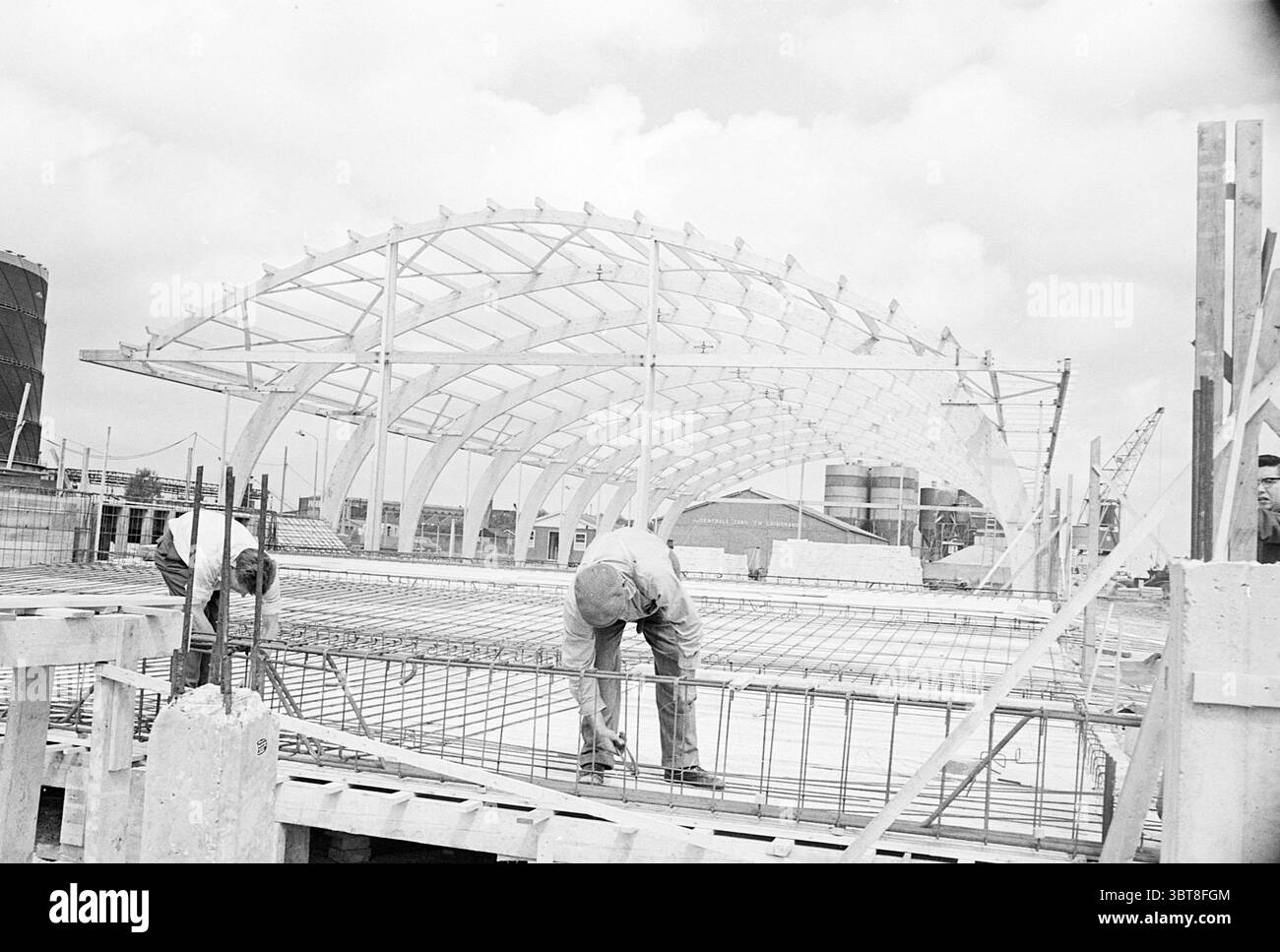 Gemüseauktion, Whizgle News, Dutch Desk, Niederlande, 1950 - 2000 am 11-07-1963. Dies sind die Themen im Bild. In der Szene sind mehrere Personen an verschiedenen Bauaufgaben auf einem Rahmen eines Gebäudes in Entwicklung beteiligt. Die Struktur verfügt über ein modernes, geschwungenes Dachdesign mit einer Reihe von geschwungenen Elementen, die ihm ein luftiges Gefühl verleihen und sich von den schweren Materialien um sie herum abheben. Die Arbeiter konzentrieren sich auf ihre Aufgaben: Ein Mann beugt sich über ein Stahlgitter und passt die Platzierung des Metalls akribisch an, während ein anderer möglicherweise in der Nähe steht Stockfoto
