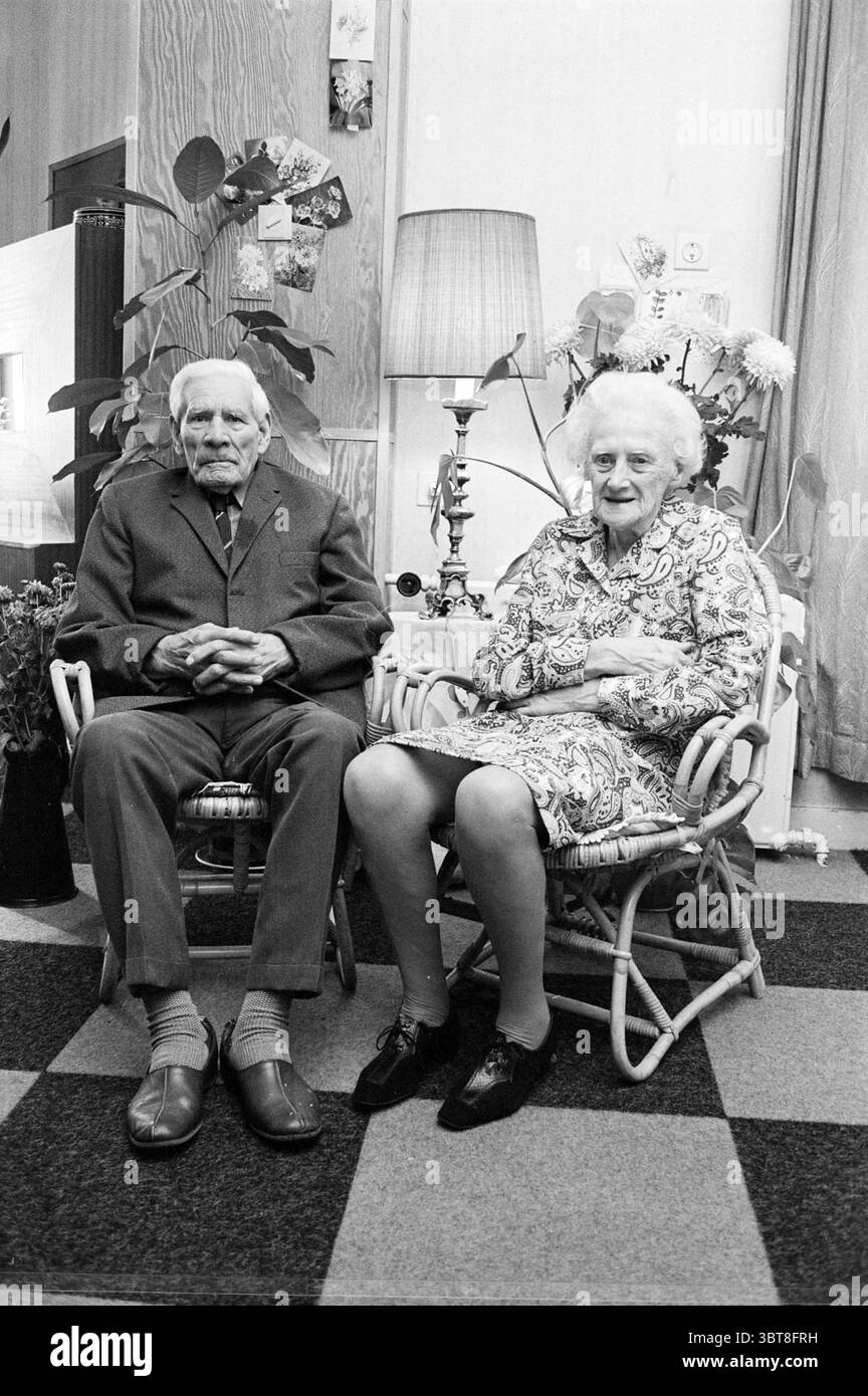 50-jähriges Paar de Bode Couples, Whizgle News, Dutch Desk, Niederlande, 1950 - 2000 am 19.09.1972. Dies sind die Themen im Bild. Die Szene zeigt ein älteres Paar, das nebeneinander in einer gemütlichen Innenumgebung sitzt. Sie befinden sich in einem Paar Korbsessel mit weichem, strukturiertem Stoff, der die Sitze bedeckt. Der Mann, gekleidet in einem maßgeschneiderten grauen Anzug, strahlt ein Gefühl von würde aus. Sein zurückgeschliffenes Haar ist weiß, und er hat einen ausgeglichenen, nachdenklichen Ausdruck. Er trägt dunkle Schuhe, ergänzt durch helle Socken. Neben ihm trägt die Frau ein florales Kleid, Stockfoto