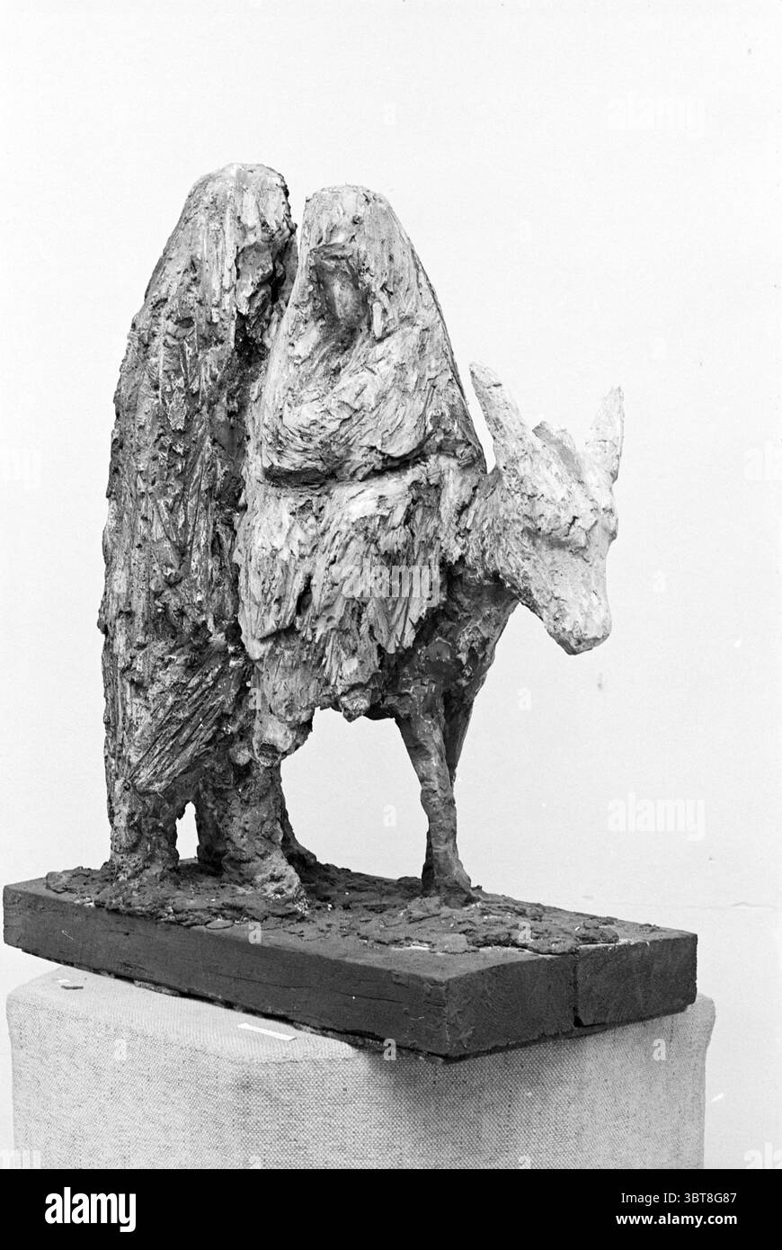 Skulptur Joseph and Mary on Esel, Whizgle News, Dutch Desk, Niederlande, 1950 - 2000 im Jahr 1968. Diese Themen werden in der Abbildung angezeigt. Die Szene zeigt eine markante Skulptur, die mit ihrer strukturierten Oberfläche und ihrer einzigartigen Form Aufmerksamkeit auf sich zieht. Die zentrale Figur ähnelt einem Tier, wahrscheinlich einer Ziege, mit ausgeprägten Merkmalen wie langen Ohren und einer ausgeprägten Schnauze. Der Körper ist mit einer rauen, fast organischen Textur gefertigt, die sowohl die Stärke als auch die Verletzlichkeit der Kreatur andeutet. Das Tier umgibt zwei abstrakte Figuren, deren Formen mit dem Körper der Ziege verflochten sind. Diese Stockfoto