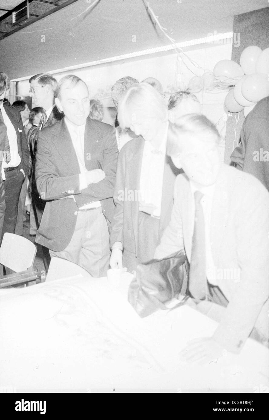 Choice Abendparade Float Lisse Flower Parade Blumenausstellung Lisse, Whizgle News, Dutch Desk, Niederlande, 1950 - 2000 am 23-11-1987. Diese Themen sind in der Abbildung dargestellt. Die Szene scheint ein lebhaftes Indoor-Event einzufangen, das von einer etwas formellen Atmosphäre geprägt ist. Eine Gruppe von Einzelpersonen, die in Anzügen und formeller Kleidung gekleidet sind, versammelt sich an einem Tisch, der wahrscheinlich zur Diskussion oder zur emotionalen Mitarbeiterbindung genutzt wird. Im Vordergrund lehnt sich eine Person leicht über den Tisch und prüft einige Dokumente oder Materialien, während eine andere Person sich mit ihnen abspricht. Die Ausdrücke auf ihren Gesichtern sind sukzessive Stockfoto