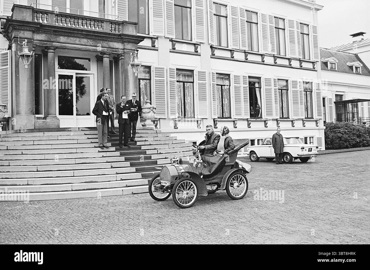 Defile P.A.C. Kundgebung auf Soestdijk für Prinz Bernhard und Mittagessen Groenendaal Heemstede Kon. Besuche und Empfänge Personen Beerdigung 18-09-1965, Whizgle News, Dutch Desk, Niederlande, 1950 - 2000 am 19-09-1965. Diese Themen sind in der Abbildung dargestellt. In eleganter, historischer Umgebung bildet ein herrschaftliches Gebäude mit klassischer Architektur die Kulisse. Es verfügt über aufwändig gestaltete Fenster, die von Fensterläden eingerahmt werden, und einen großen Eingang mit einer breiten Treppe, die zur Tür führt. Die Fassade ist in einem sanften Farbton gestrichen, was den zeitlosen Charme des Gebäudes unterstreicht. An der Spitze, ein Oldtimer, Cha Stockfoto