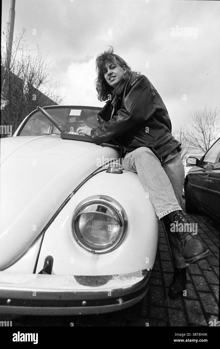 Systemadministrator HD, Whizgle News, Dutch Desk, Niederlande, 1950 - 2000 am 20-03-1995. Dies sind die Elemente im Bild. In der Szene sitzt eine Person auf der Vorderseite eines weißen Oldtimers, wahrscheinlich eines klassischen Volkswagen Käfers. Die Person hat schulterlange Haare, die in lockeren Wellen gestylt sind, und trägt eine schwarze Lederjacke, die für eine ausgefallene Atmosphäre sorgt. Sie sind auch in Denim-Jeans erhältlich, die durch robuste schwarze Stiefel ergänzt werden, die einen lässigen, aber starken Stil versprechen. Der Hintergrund zeigt eine Mischung aus Bäumen und Gebäuden, mit einem leicht bewölkten Himmel, der ein weiches, diffuses Licht erzeugt und einen Mo erzeugt Stockfoto
