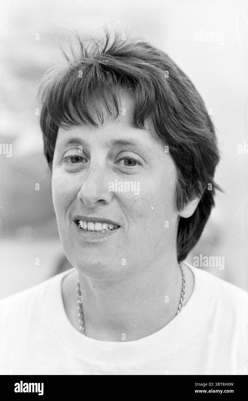 Mrs. Metz Emanzipationskomitee Velsen und Mrs. By. Eck Persons Velsen, Whizgle News, Dutch Desk, Niederlande, 1950 - 2000 am 11-05-1989. Das Bild enthält diese Themen. Eine Frau mit kurzen, dunklen Haaren ist der Mittelpunkt der Szene. Ihr Haar ist leicht zerzaust, mit sanften Wellen, die ihr Gesicht umrahmen. Sie hat einen sanften Ausdruck, der von einem subtilen Lächeln geprägt ist, das Wärme vermittelt. Ihr Teint wirkt glatt und hell, und ihre Augen sind hell, was auf ein Gefühl der Zugänglichkeit hindeutet. Was die Kleidung angeht, trägt sie ein einfaches, helles Hemd, das im Kontrast zu den dunkleren Tönen ihres h steht Stockfoto