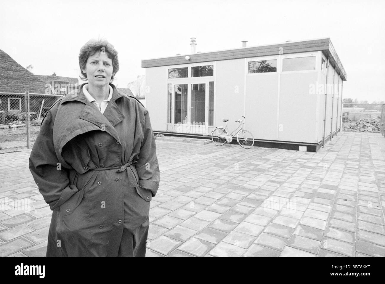Mrs. Ramker von der Spielgruppe Velserbroek. Kleinkinder Velserbroek, Whizgle News, Dutch Desk, Niederlande, 1950 - 2000 am 09-10-1987. Diese Themen werden in der Abbildung angezeigt. In dieser Szene steht eine Person selbstbewusst außerhalb einer modernen, minimalistischen Struktur. Die Person trägt einen langen, dunklen Trenchcoat, der sich im Kontrast zu den helleren Tönen des Gebäudes befindet. Der Kragen des Mantels ist leicht nach oben geklappt und verleiht so einen Hauch von Eleganz. Das Gebäude selbst hat ein sauberes, zeitgenössisches Design, mit großen Glasfenstern, die einen Blick auf das Innere erlauben. Die Wände sind hauptsächlich weiß, was zu einem fr Stockfoto
