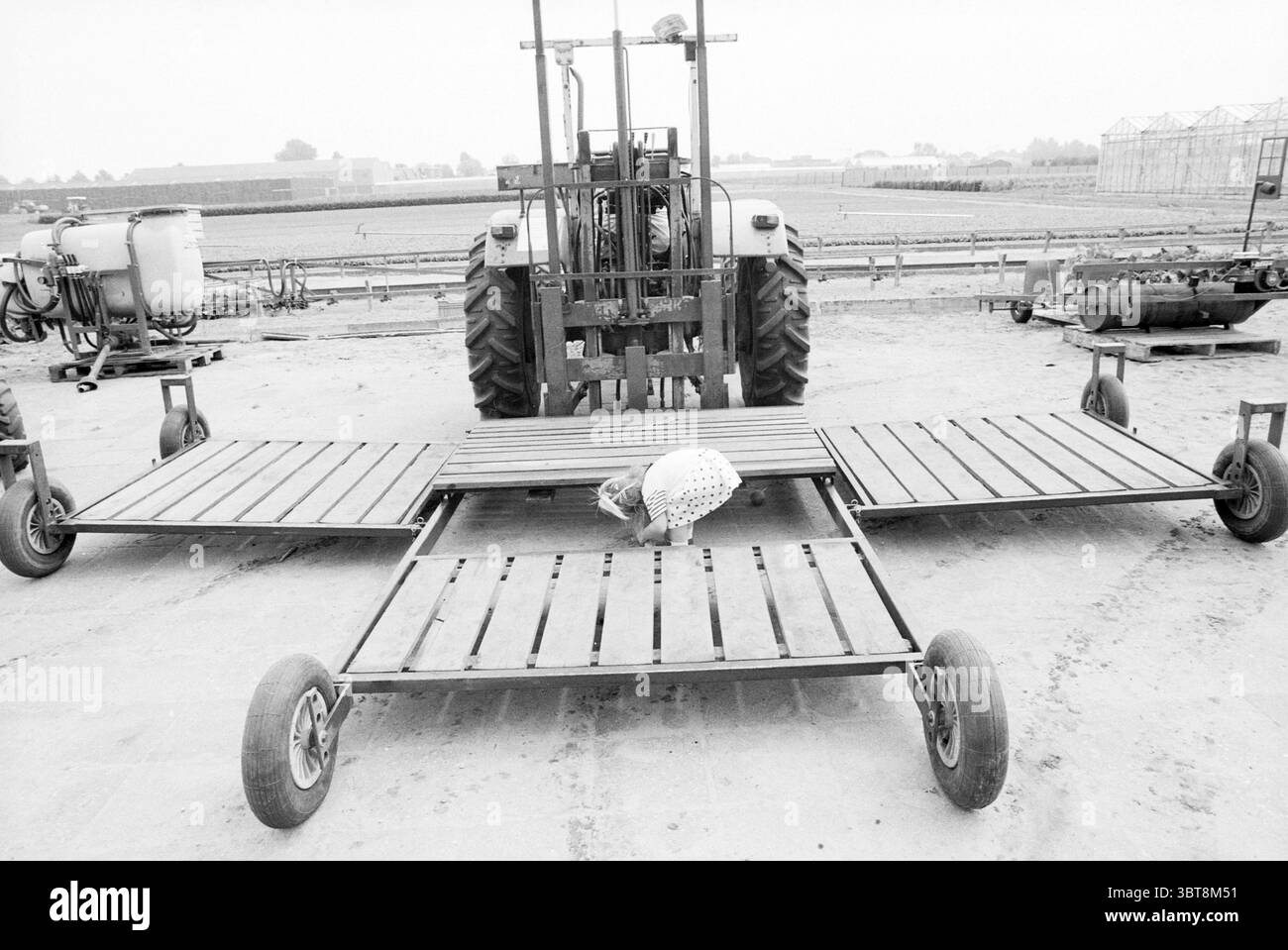 Tag der offenen Tür der landwirtschaftlichen Unternehmen in Hillegom Hillegom, Whizgle News, Dutch Desk, Niederlande, 1950 - 2000 am 31-07-1992. Dies sind die Elemente im Bild. Die Szene wird von einem großen, schweren Traktor dominiert, dessen robuste Reifen auf Festigkeit und Langlebigkeit hinweisen. Der Traktor sitzt in der Mitte und wird von einem metallischen Arbeitsgerät flankiert, das wie ein Anbaugerät für den landwirtschaftlichen Einsatz aussieht. Dieses Arbeitsgerät wird auf beiden Seiten nach außen ausgefahren und verfügt über stabile Holzplattformen aus Leisten. Die Oberfläche des Holzes zeigt ein verwittertes Aussehen, was auf die Exposition gegenüber den Elementen hinweist, und ist lackiert Stockfoto