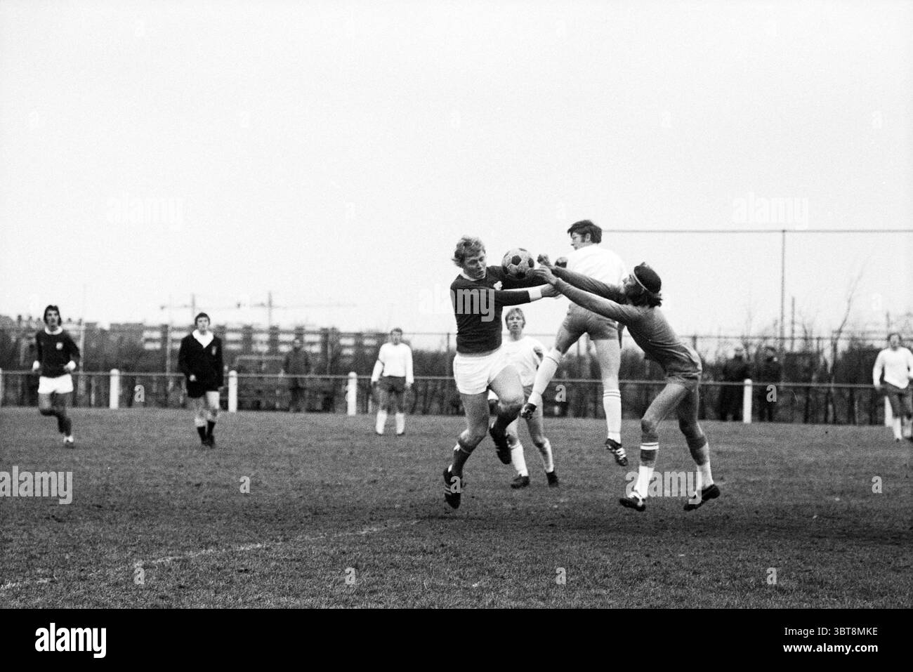 VSV - DTS Football V.S.V. Velsen Stormvogels, Whizgle News, Dutch Desk, Niederlande, 1950 - 2000 am 12.12.1971. Das Bild enthält diese Themen. Die Szene fängt einen dynamischen Moment eines Fußballspiels auf einem grasbewachsenen Feld ein, in dem die Atmosphäre voller Energie und Konkurrenz ist. Im Vordergrund stehen zwei Spieler im Mittelpunkt des Geschehens. Der eine, der in einem roten Trikot und weißen Shorts gekleidet ist, springt nach vorne und dehnt seinen Körper aus, um den Ball zu gewinnen. Sein Gesicht zeigt Entschlossenheit, und sein Haar ist von der Anstrengung des Stücks entrüttelt. Er wird von einem Torhüter in Grau, W, bestritten Stockfoto