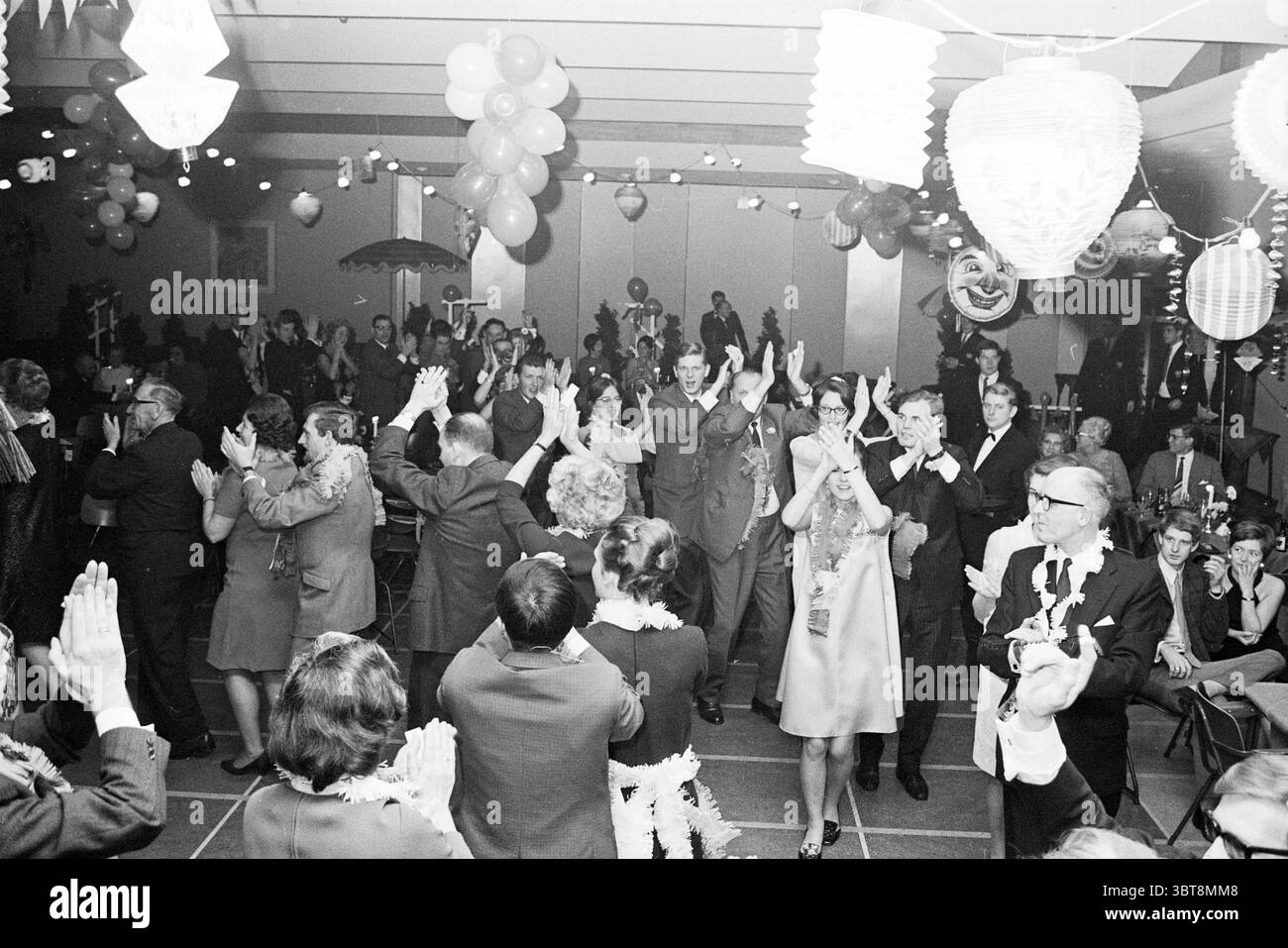 Partyabend Nutsspaarbank Parties Nuts united Savings Banks, Whizgle News, Dutch Desk, Niederlande, 1950 - 2000 am 02-12-1967. Das Bild enthält diese Themen. Die Szene ist lebendig und voller Feiern. Die Komposition fängt ein lebhaftes Treffen mit verschiedenen Gruppen von Menschen ein, die sich mit Tanz und Unterhaltung beschäftigen. Die Menge ist in einer Reihe formeller Kleidung gekleidet, darunter Anzüge und elegante Kleider, die eine Mischung aus klassischen Stilen und Farben bieten. Bunte Ballons schweben über den Teilnehmern und schaffen eine festliche Atmosphäre. Die Laternen hängen von der Decke und geben ein warmes Licht Stockfoto