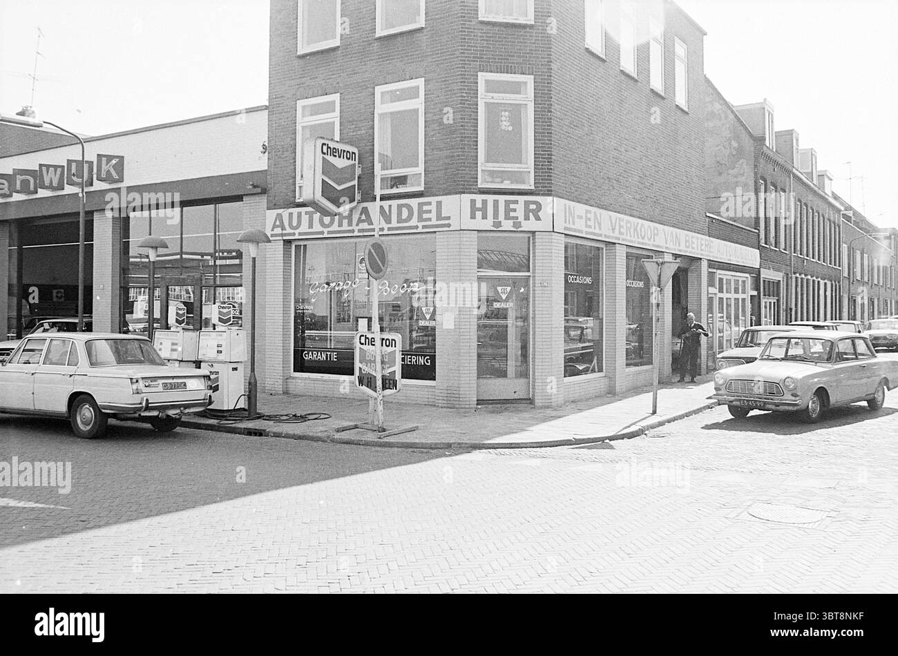 Erw. Jugendzentrum d'Appelaer Ext. Jugendzentrum Kampersingel Ext. Garage Amsterdamsevaart Exterior Haarlem Amsterdamsevaart Niederlande, Whizgle News, Dutch Desk, Niederlande, 1950 - 2000 am 22-03-1972. Die Abbildung zeigt diese Themen. Die Szene zeigt eine Straßenecke in urbaner Umgebung, die durch eine Mischung aus flachen Gebäuden und Ladenfronten gekennzeichnet ist. Die markante Struktur im Vordergrund ist ein zweistöckiges Gebäude mit großen Fenstern, die einen Fahrzeugverkauf und Service zeigen. Das Äußere verfügt über eine schlichte, schlichte Ziegelfassade, die in neutralen Tönen lackiert ist und einen klassischen Look verleiht. Th Stockfoto