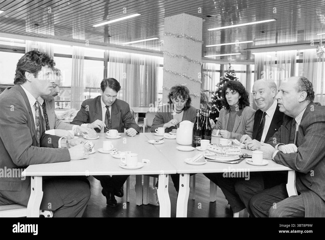 Präsentation der 25000. Damiaatje Haarlem the Netherlands, Whizgle News, Dutch Desk, Niederlande, 1950-2000, 15-12-1994. Dies sind die Elemente im Bild. Die Szene entfaltet sich in einem modernen Konferenzraum mit großen Fenstern, die viel natürliches Licht hereinlassen und den Raum mit einem sanften Licht beleuchten. Das Zimmer verfügt über eine helle Holzdecke und eine minimalistische Einrichtung, die ihm eine saubere und moderne Atmosphäre verleiht. Um einen geräumigen weißen Tisch sitzen sieben Personen, die sich in lebhaften Gesprächen unterhalten. Die Gruppe scheint eine Mischung aus Männern und Frauen zu sein, mit einem bemerkenswerten Fortsatz Stockfoto