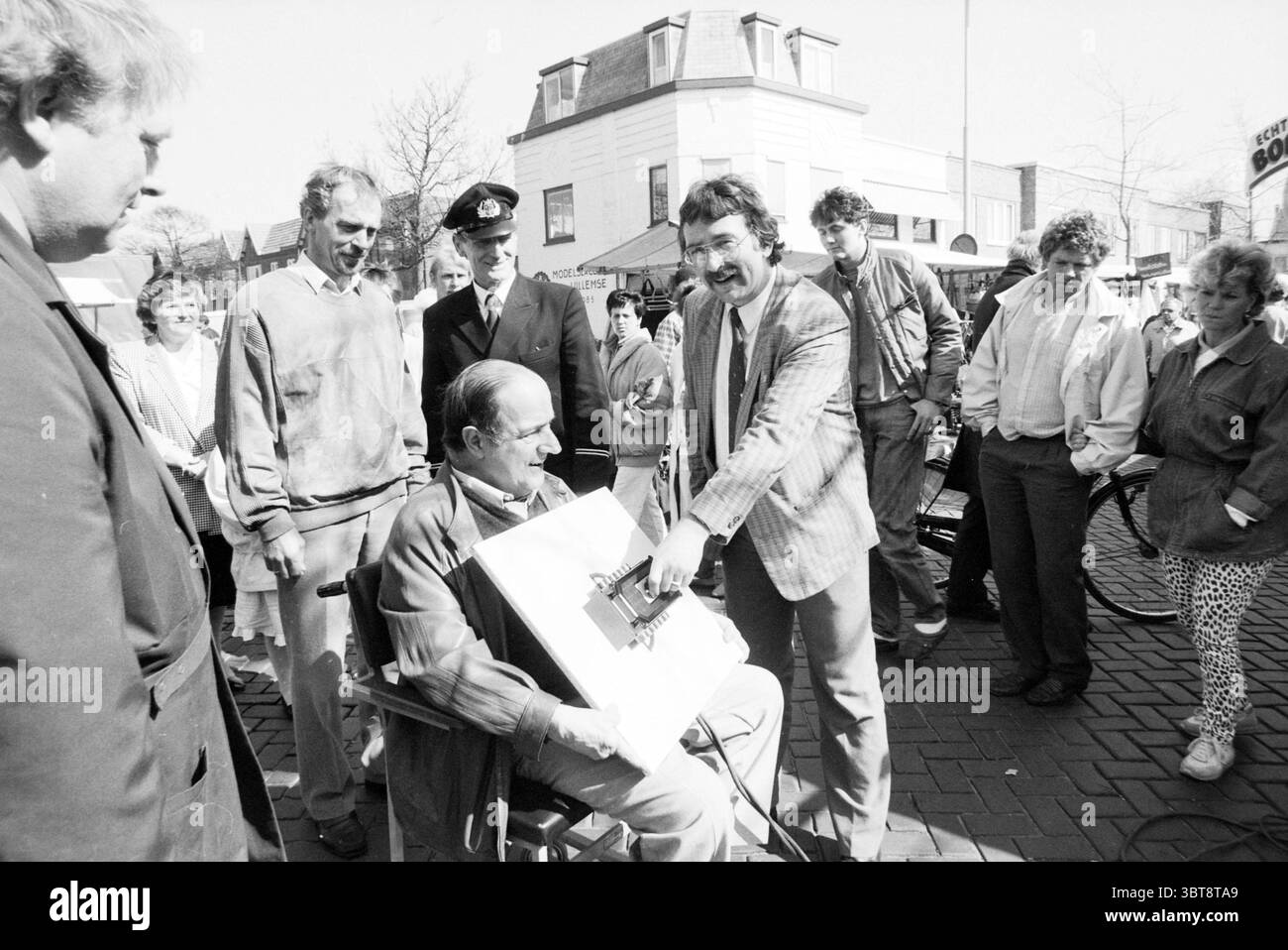 Inbetriebnahme des Strommarktes Florisstraat Inbetriebnahme Haarlem Floresstraat, Whizgle News, Dutch Desk, Niederlande, 1950 - 2000 am 30-03-1989. Dies sind die Themen im Bild. Eine lebhafte Straßenszene entfaltet sich, in der sich eine Gruppe von Individuen um eine zentrale Figur versammelt. Im Vordergrund bewegt sich ein Mann in einem Anzug animiert und zieht die Aufmerksamkeit der Zuschauer auf sich. Er zeigt ein breites Lächeln und strahlt Begeisterung aus, während er ein faszinierendes Objekt präsentiert, das auf ein Element der Überraschung oder Unterhaltung hinweist. An seiner Seite erscheint ein sitzender Mann mit kurzen Haaren verwickelt Stockfoto