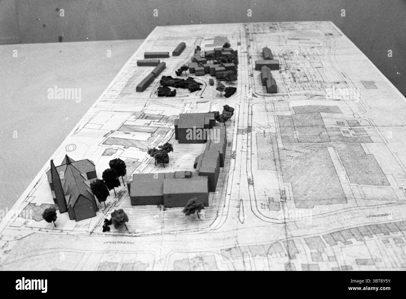 Modell Olympiaweg Hillegom Hillegom Modell Hillegom Olympiaweg, Whizgle News, Dutch Desk, Niederlande, 1950 - 2000 am 12-09-1979. Das Bild enthält diese Themen. Die Szene zeigt ein detailliertes Architekturmodell auf einer Ebenen Fläche, das ein geplantes Layout von Gebäuden und Landschaft zeigt. Das Modell selbst ist aus einfachen geometrischen Formen gefertigt, die verschiedene Strukturen wie Häuser und größere Gebäude repräsentieren, und ist in gedämpften Tönen – meist Grau- und Brauntönen – bemalt, was ihm eine minimalistische Atmosphäre verleiht. Um das Modell herum sind kleine, geformte Bäume, auch in Grundformen, die einen Touch o hinzufügen Stockfoto