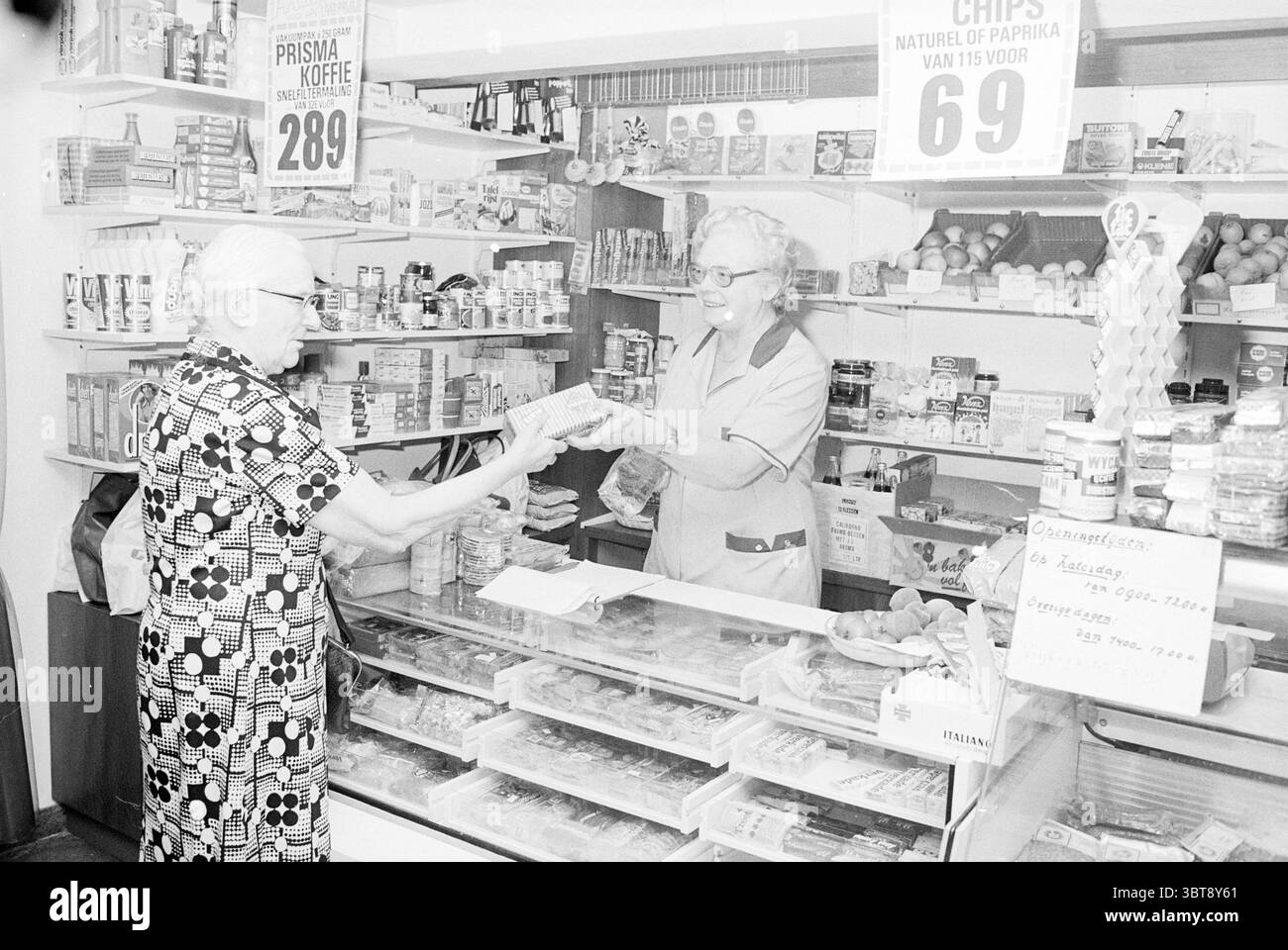 Lebensmittelgeschäft Breezicht IJmuiden Geschäfte und Kioske IJmuiden Niederlande, Whizgle News, Dutch Desk, Niederlande, 1950 - 2000 am 21-06-1979. Das Bild enthält diese Themen. Die Szene zeigt das Innere eines kleinen, hübschen Lebensmittelgeschäfts, der sich durch seinen nostalgischen Charme auszeichnet. Helle weiße Wände und Holzregale säumen den Raum, gefüllt mit verschiedenen Dosenwaren und verpackten Snacks, organisiert, aber leicht übersichtlich angeordnet. In den Regalen befinden sich verschiedene Gegenstände, darunter leuchtende Dosen und Boxen, die Farbtupfer vor dem neutralen Hintergrund bieten. Im Vordergrund ein Ol Stockfoto