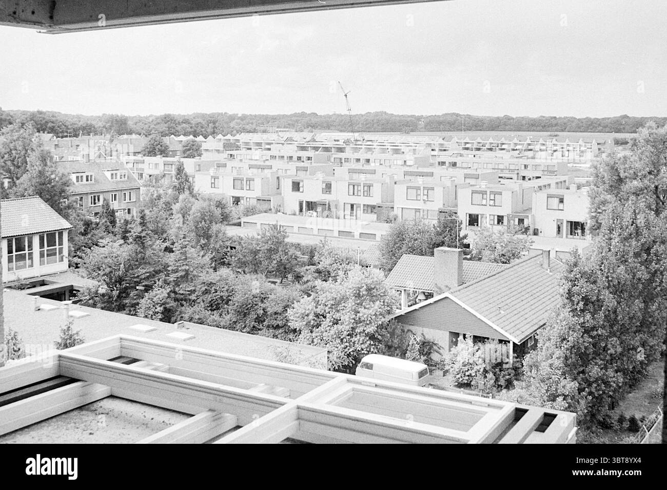 Neubau Häuser in allen Arten von Formen., Whizgle News, Dutch Desk, Niederlande, 1950 - 2000 am 18-07-1973. Das Bild enthält diese Themen. Die Szene zeigt eine weitläufige Wohngegend von oben aus, die eine Anordnung von Häusern und Grünflächen zeigt. Die Gebäude sind überwiegend modern im Design, mit flachen Dächern und rechteckigen Formen, mit einer Mischung aus hellen und dunklen Farbtönen, die einen einheitlichen architektonischen Stil suggerieren. Der Vordergrund bietet einen Blick auf Dächer, von denen einige mit Schindeln und andere mit kontrastierenden Materialien dekoriert sind, während entlang ein Baugerüst zu sehen ist Stockfoto