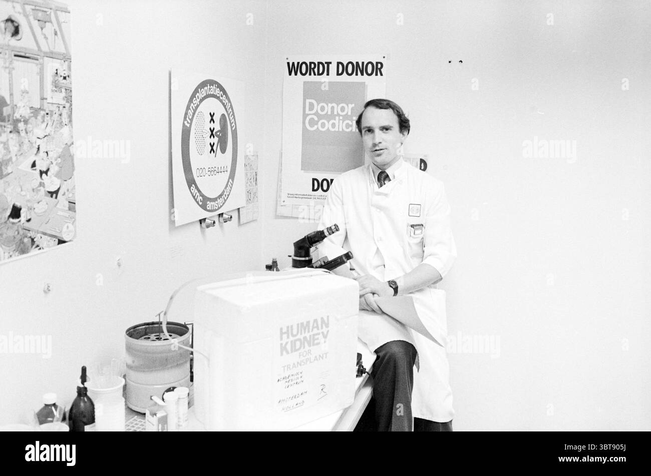 Dr. Strongers zur Nierentransplantation AMC Amsterdam. Medizin Heilmethode Amsterdam Niederlande, Whizgle News, Dutch Desk, Niederlande, 1950 - 2000 am 21-04-1985. Diese Themen werden in der Abbildung angezeigt. In einer klinischen Umgebung sitzt ein Mann in einem weißen Labormantel neben einem großen, quadratischen Behälter, der mit der Aufschrift „MENSCHLICHE NIERENTRANSPLANTATION“ gekennzeichnet ist. Er hat ordentlich gekämmtes Haar und scheint konzentriert zu sein und vermittelt ein Gefühl von Professionalität und Ernsthaftigkeit. Der Hintergrund zeigt eine weiße Wand mit verschiedenen Plakaten, die symbolische Grafiken in Bezug auf die Organspende enthalten. Für ihn Stockfoto