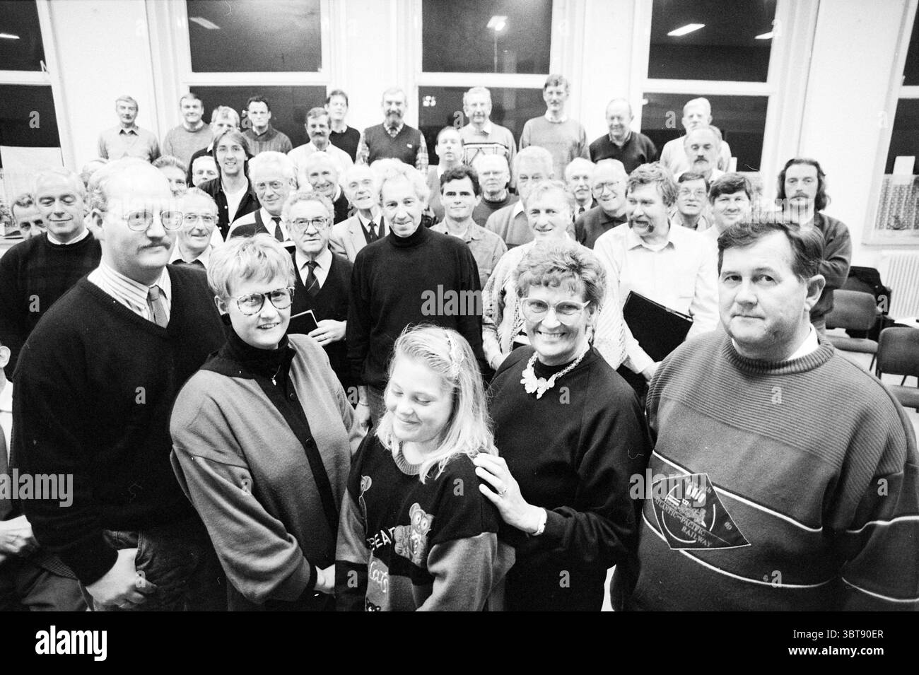 Freunde des Zandvoort Männerchors Zandvoort, Whizgle News, Dutch Desk, Niederlande, 1950 - 2000 am 11-11-1991. Die Abbildung zeigt diese Themen. Die Szene zeigt eine große Gruppe von Einzelpersonen, die sich versammelt haben und ein Gefühl von Gemeinschaft und Kameradschaft schaffen. Die Menschen variieren im Alter, aber die Mehrheit scheint mittleren Alters oder älter zu sein, darunter einige jüngere Personen. Die Gesichtsausdrücke reichen von Lächeln bis hin zu durchdachten Blicken, was zu einer Atmosphäre der Freundlichkeit und Verbundenheit beiträgt. Die Umgebung scheint ein Innenraum zu sein, möglicherweise eine Gemeindehalle, mit großen Flächen Stockfoto