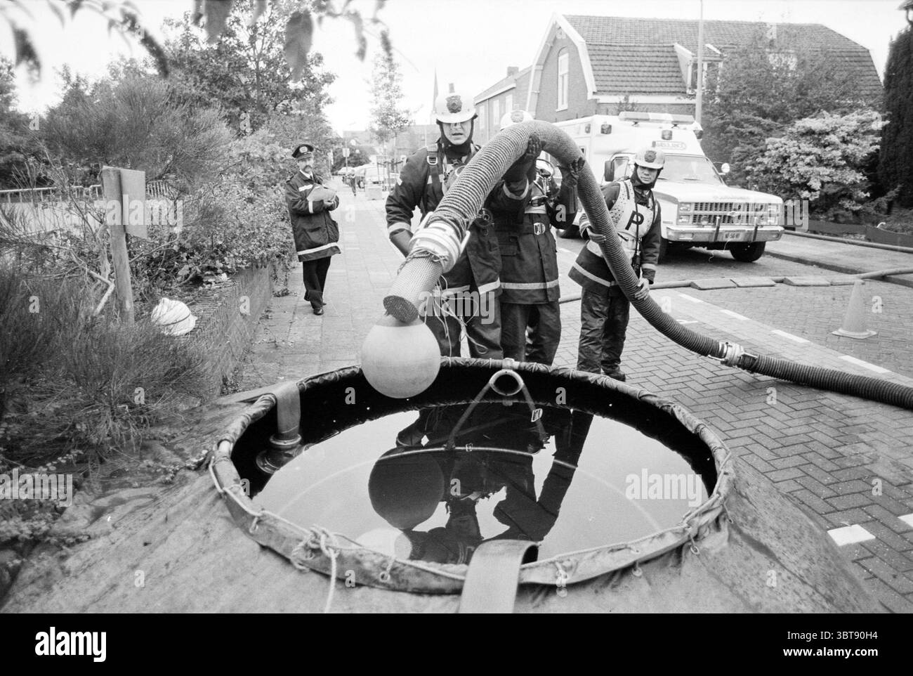 Feuerwehrwettbewerb Haarlemmer Hout Haarlem the Netherlands, Whizgle News, Dutch Desk, Niederlande, 1950 - 2000 am 21.09.1990. Das Bild enthält diese Themen. Die Szene zeigt eine Gruppe von Feuerwehrleuten, die in der Nähe eines großen, dunklen Wasserpools operieren, der sich in einem kreisförmigen, erhöhten Gebäude befindet. Die Feuerwehrleute, die in Standardfeuerausrüstung mit Helmen gekleidet sind, sind konzentriert und methodisch in ihrem Handeln. Eine Person hält einen dicken Gummischlauch, der sich zur Wasseroberfläche erstreckt und die Flüssigkeit wahrscheinlich für einen bestimmten Zweck absaugt. Das Settin Stockfoto