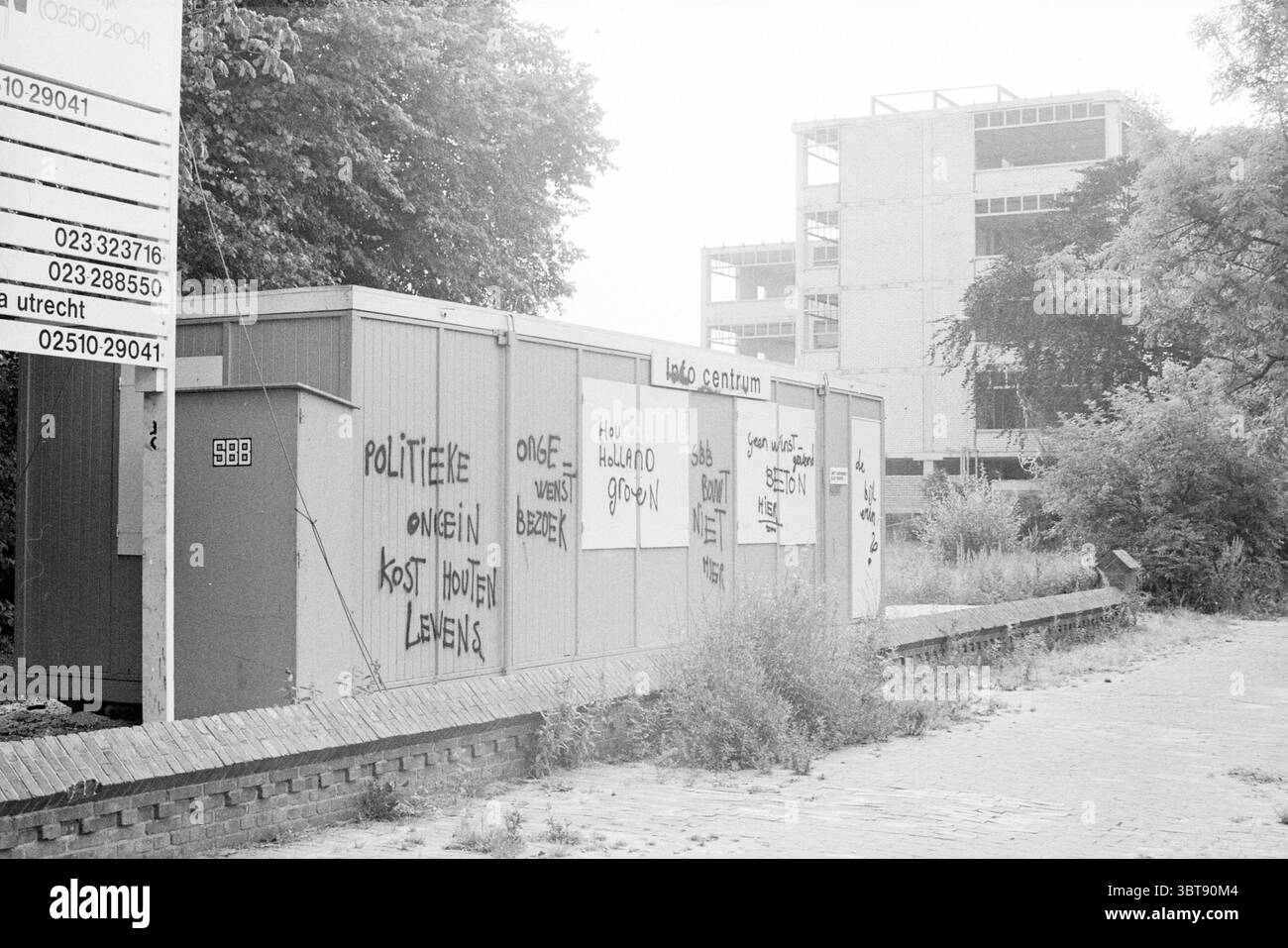 Defacing Information Stand Zijlweg Demolitions Haarlem Zijlweg the Netherlands, Whizgle News, Dutch Desk, Niederlande, 1950 - 2000 am 12-08-1984. Diese Themen werden in der Abbildung angezeigt. Im Hintergrund befindet sich ein teilweise gebautes Gebäude, das sich durch seine Skelettstruktur auszeichnet, die auf unfertige Materialien und ein freiliegendes Gerüst hinweist. Um diese Baustelle herum wird der Vordergrund von einer Reihe von Containern oder Bauwerken dominiert, die wahrscheinlich einem vorübergehenden Zweck dienen. Diese Behälter sind deutlich mit Graffiti gekennzeichnet, mit einem fetten, schwarzen Schriftzug, der auf Soci hinweist Stockfoto