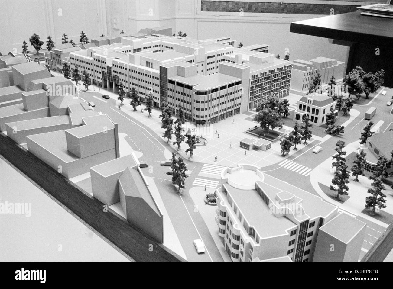 Model Houtplein Model Haarlem Houtplein The Netherlands, Whizgle News, Dutch Desk, Niederlande, 1950 - 2000 am 05-12-1984. Diese Themen werden in der Abbildung angezeigt. Die Szene zeigt ein detailliertes Architekturmodell, das ein städtisches Layout zeigt. Im Vordergrund dient ein kreisförmiger Kreisverkehr als zentrales Merkmal, umgeben von Miniaturbäumen und kleinen Fahrzeugen, die den Verkehrsfluss anzeigen. In der Nähe sind Gebäudebündel in unterschiedlichen Höhen und geometrischen Formen dargestellt, was ein Gefühl von Modernität und Stadtplanung schafft. Die Strukturen sind überwiegend helle Farbtöne, hauptsächlich weiß und gra Stockfoto