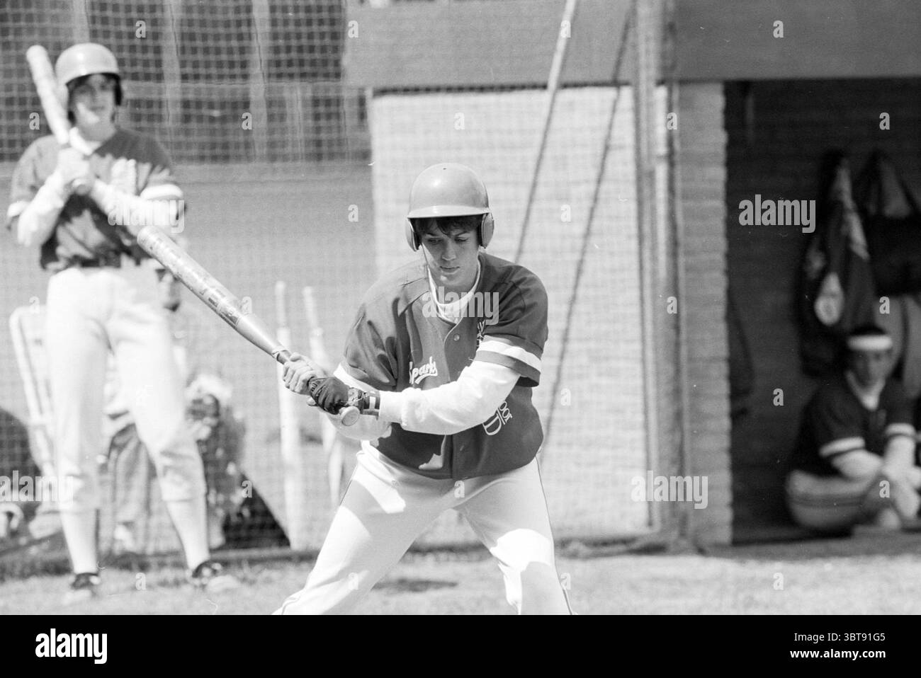 Softball Sparks - Bloemendaal, Whizgle News, Dutch Desk, Niederlande, 1950 - 2000 am 15-06-1991. Dies sind die Elemente im Bild. Die Szene entfaltet sich an einem hellen, sonnigen Tag auf einem Baseballfeld. Das Gras ist ein leuchtendes Grün, das sich von den Erdtönen des Innenfeldes abhebt. Ein junger Spieler steht auf dem Teller, bereit zum Schaukeln, gekleidet in einem knallroten Trikot und einer weißen Hose. Sein Helm, ein glänzendes Rot, trägt zum Teamgeist bei. Seine Haltung zeigt Konzentration und Entschlossenheit, wobei beide Hände den Schläger fest greifen. Hinter ihm lehnt sich ein zweiter Spieler gegen den du Stockfoto