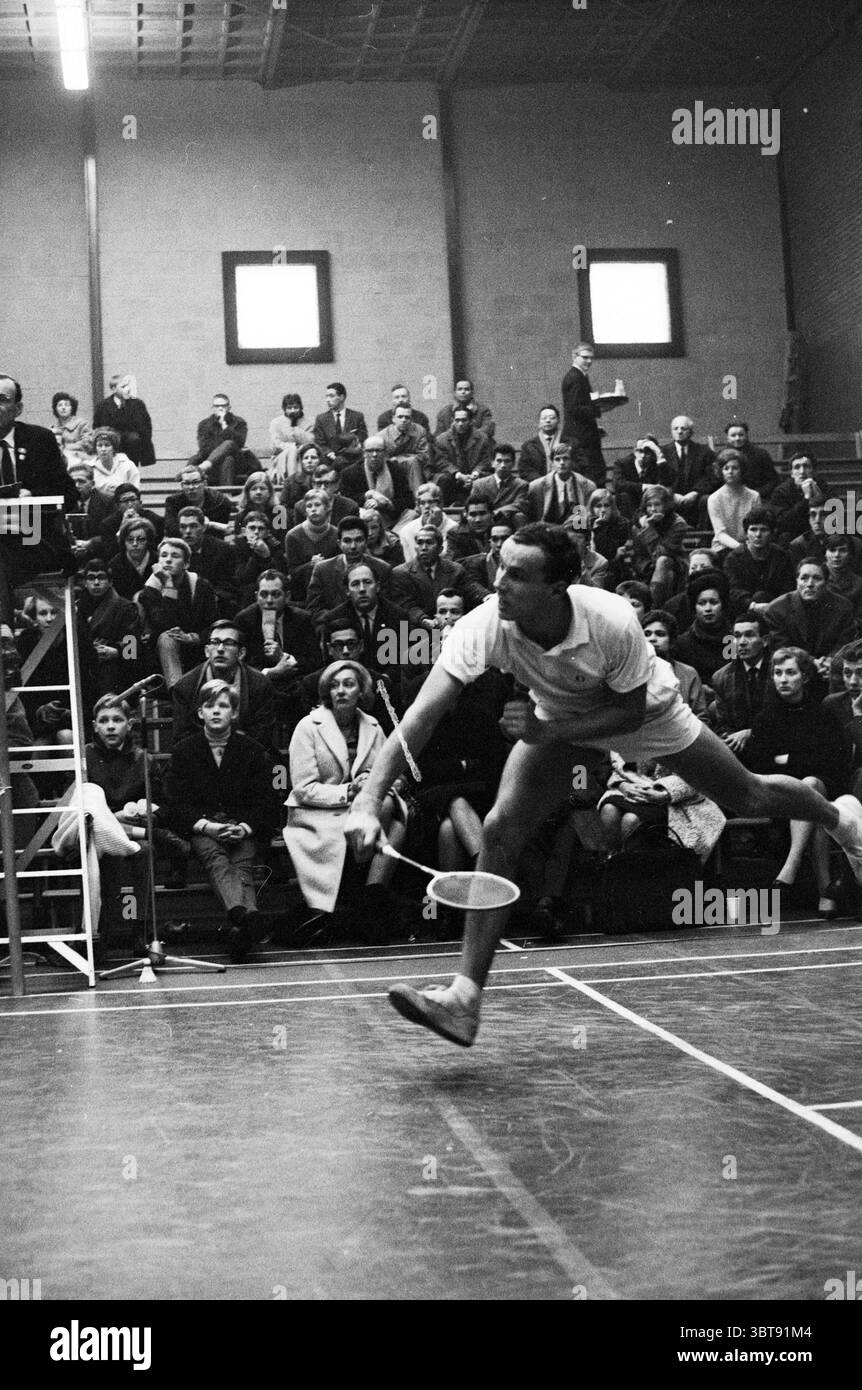 Badminton im Duinwijckhal des Badmintonclubs Duinwijck Haarlem Badmintonpad Niederlande., Whizgle News, Dutch Desk, Niederlande, 1950 - 2000. Das Bild enthält diese Themen. In einer dynamischen Hallensportanlage wird ein männlicher Athlet während des Squashspiels in der Mitte der Action gefangen. Er trägt ein helles, sportliches Outfit, bestehend aus einem kurzärmeligen Hemd und Shorts, die seine Bewegung hervorheben. Sein Körper lehnt sich nach vorne, während er sich springt, mit einem Fuß in der Luft und dem anderen fest auf dem Boden, was Agilität und Konzentration zum Ausdruck bringt. Der Schläger in seiner Hand ist bereit, den Ball zu schlagen, Rev Stockfoto