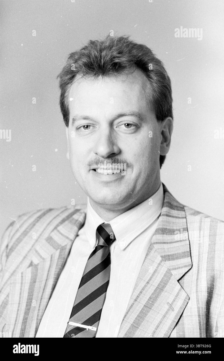 Porträt Fred Postma, Whizgle News, Dutch Desk, Niederlande, 1950 - 2000 am 06-04-1989. Das Bild enthält diese Themen. Ein Mann mit einem selbstbewussten Lächeln wird in einem professionellen Umfeld dargestellt. Er hat einen hellbraunen Schnurrbart, der zu seinem ordentlich gestylten Haar passt, das ein paar dunkler ist. Er trägt einen gestreiften Anzug in gedämpften Tönen mit einem Blazer, der vor einem schlichten Hintergrund sichtbar ist. Die Streifen im Material sorgen für eine dezente Textur und ein visuelles Interesse. Sein weißes Hemd bildet einen scharfen Kontrast zum Anzug, und seine Krawatte hat abwechselnde dunkelrote und marineblaue Streifen, die mit dem gesamten Mond harmonieren Stockfoto