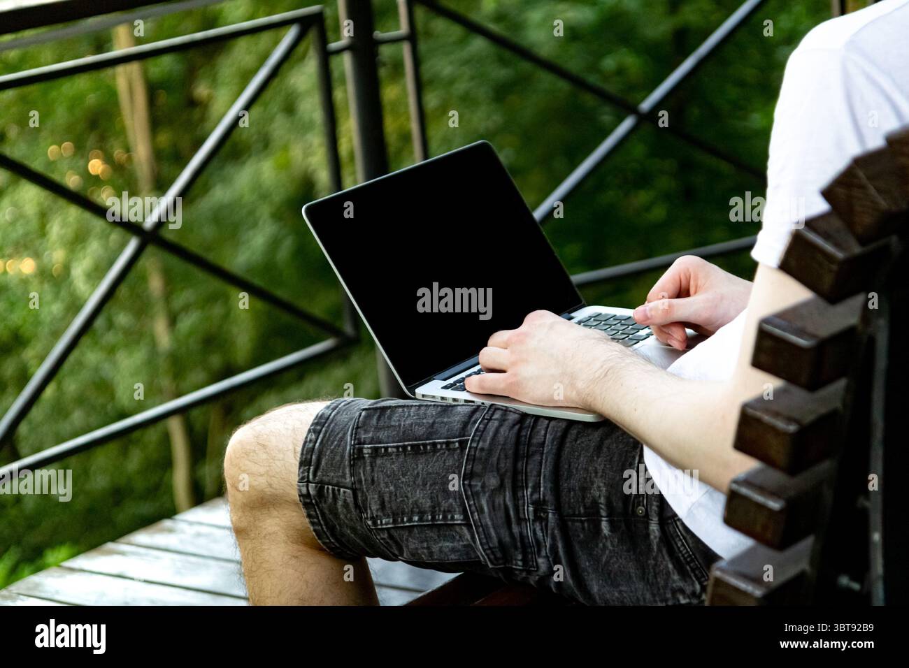 Konzentrieren Sie sich auf den Laptop-Bildschirm mit leerem Platz für Fotos oder Inhalte, während ein junger Mann im legeren Outfit im Park am Computer arbeitet. Stockfoto