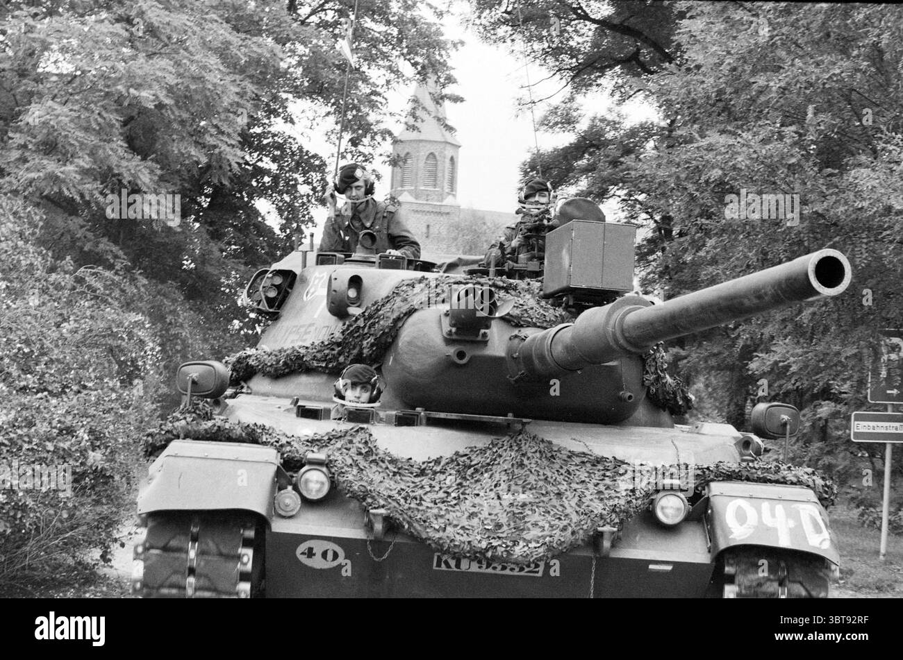 Army Exercise Atlantic Lion Germany Army, Whizgle News, Dutch Desk, Niederlande, 1950 - 2000 am 20-09-1983. Diese Themen werden in der Abbildung angezeigt. Die Szene zeigt einen Militärpanzer, der im Vordergrund sichtbar ist und mit einem Tarnnetz verziert ist, das sich in die Umgebung einfügt. Die Oberfläche des Tanks ist durch gedämpfte Grün-, Braun- und Schwarztöne gekennzeichnet, die die Texturen von Laub und Erde nachahmen. Auf dem Panzer sitzen mehrere Soldaten, die in Militäruniformen mit Helmen gekleidet sind. Ihre Ausdrucksformen sind fokussiert und spiegeln ein Gefühl von Pflicht und Wachheit wider, während sie aufsteigen Stockfoto