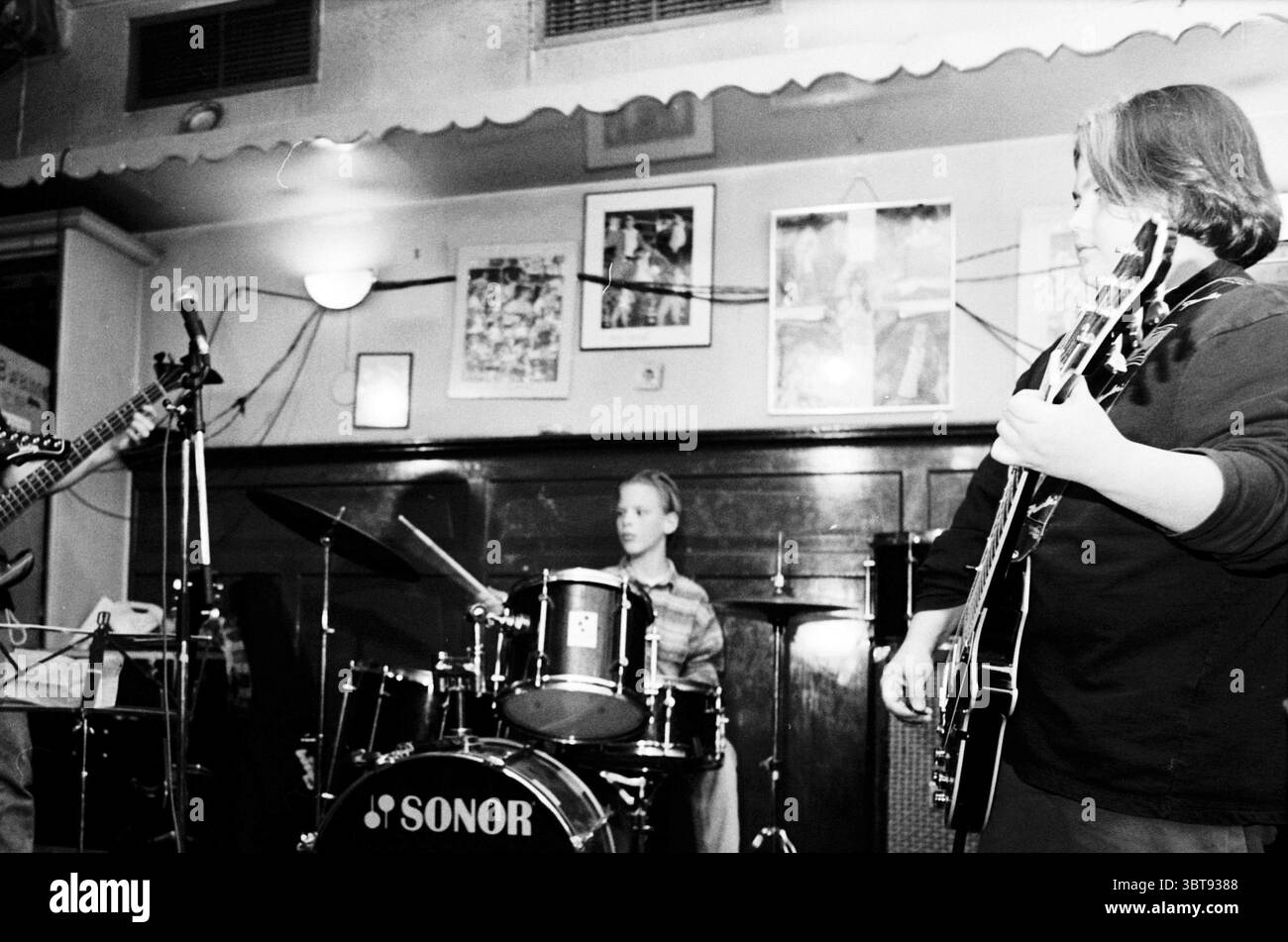 Junge Band Taverna Imperial H'lem Haarlem the Netherlands, Whizgle News, Dutch Desk, Niederlande, 1950 - 2000 am 28.02.1996. Dies sind die Themen im Bild. In einem gemütlichen, schwach beleuchteten Veranstaltungsort spielen drei junge Musiker eine lebhafte Aufführung. Das Ambiente verströmt einen nostalgischen Charme mit Retro-Dekor und gerahmten Kunstwerken an den Wänden. Warme, gedämpfte Beleuchtung schafft eine entspannte Atmosphäre, die sanfte Schatten wirft und den Ausdruck der Musiker betont. Ein Gitarrist, der links positioniert ist, konzentriert sich auf sein Instrument, wobei sich die Finger geschickt über die Saiten bewegen. Sie tragen ein lässiges Outfit, b Stockfoto