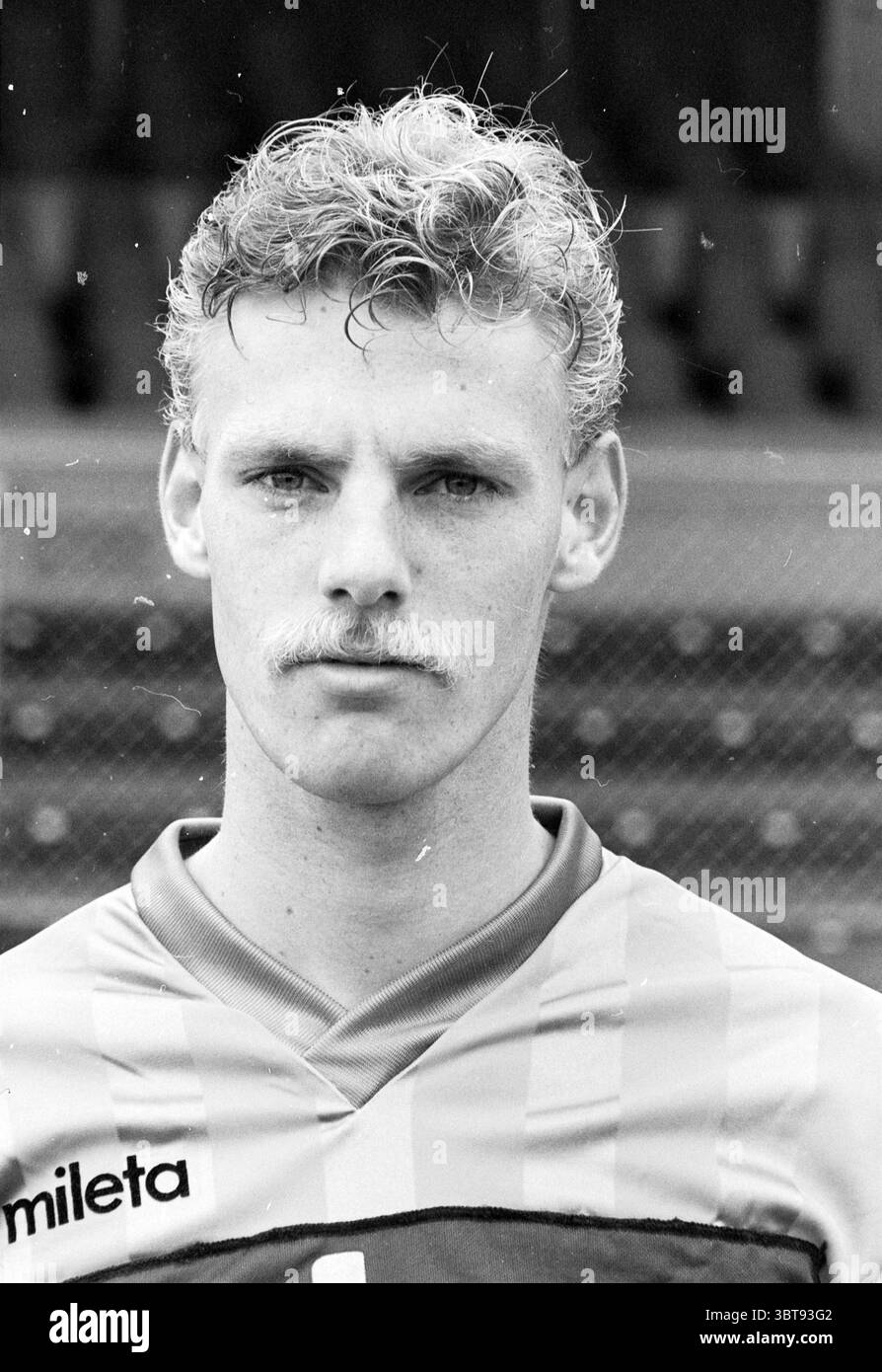 Football Telstar Gruppenfoto und Einzelfotos von Spielern, Whizgle News, Dutch Desk, Niederlande, 1950 - 2000 am 23-07-1984. Das Bild enthält diese Themen. Die Szene zeigt einen männlichen Athleten mit einer starken Präsenz. Er hat helle Haare, die in sanften Wellen gestylt sind, und einen auffälligen Schnurrbart, der seinen unverwechselbaren Look unterstreicht. Sein Ausdruck ist ernst und konzentriert, was auf Entschlossenheit hindeutet. Er trägt ein Sporttrikot mit vertikalen Streifen, überwiegend in hellen Orange- und Blautönen, die sich gegen den monochromatischen Hintergrund abheben. Das Trikot wirkt tailliert, verbessert Stockfoto