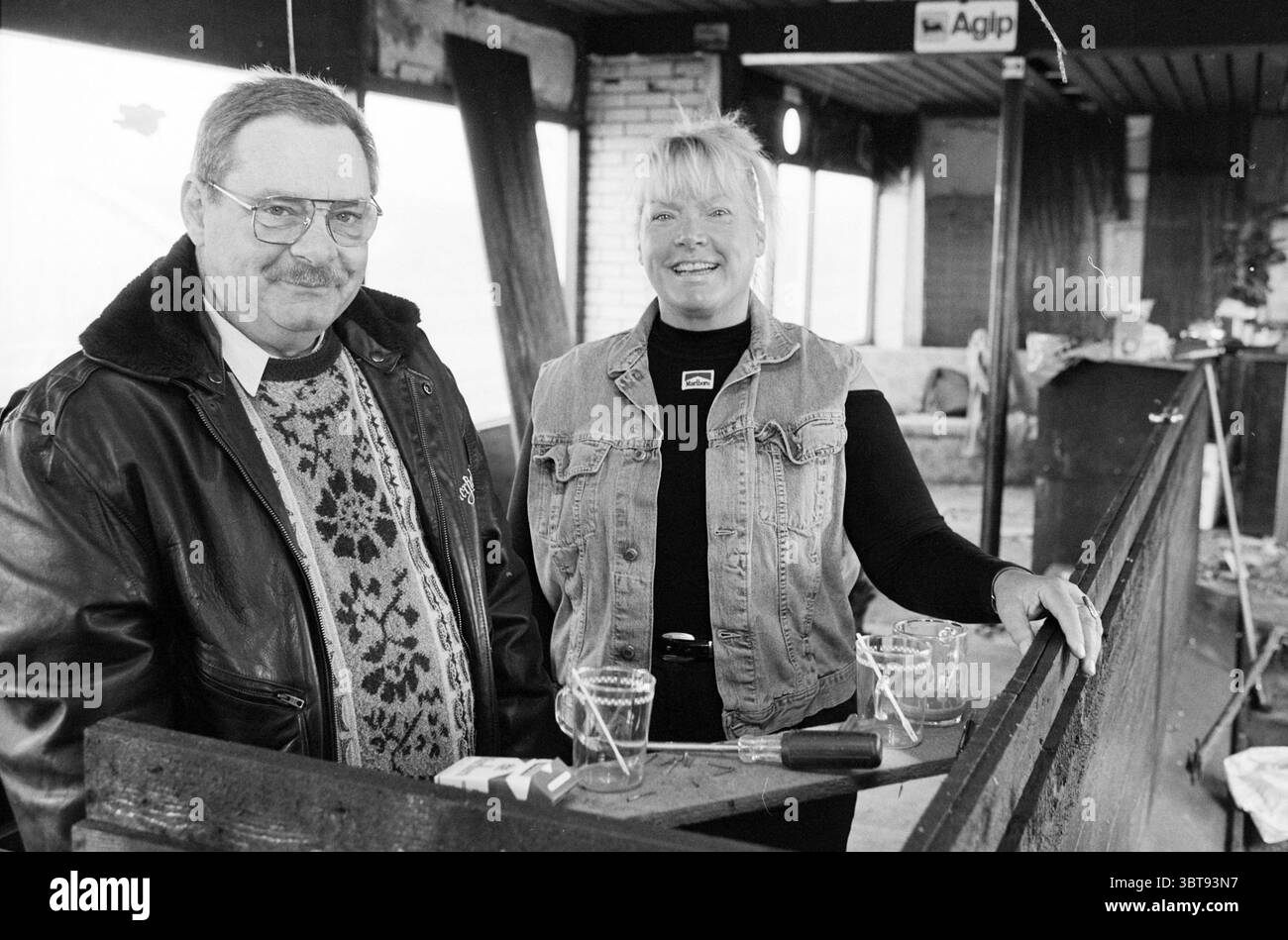 Ton Spee + Trees Huisman Zandvoort Circuit Zandvoort, Whizgle News, Dutch Desk, Niederlande, 1950 - 2000 am 20-02-1997. Das Bild enthält diese Themen. In einer gemütlichen, etwas rustikalen Inneneinrichtung stehen zwei Personen nebeneinander, die beide lächeln und Wärme ausstrahlen. Der Mann, der eine Brille und einen gemusterten Pullover unter einer dunklen Lederjacke trägt, hat ein freundliches Verhalten. Sein Schnurrbart ergänzt seinen liebenswürdigen Ausdruck. Neben ihm zeigt eine Frau mit hellfarbenen Haaren einen lässigen, aber stylischen Look, mit einer Jeansweste über einem schwarzen Oberteil. Der Hintergrund zeigt ein etwas unvollendetes A Stockfoto