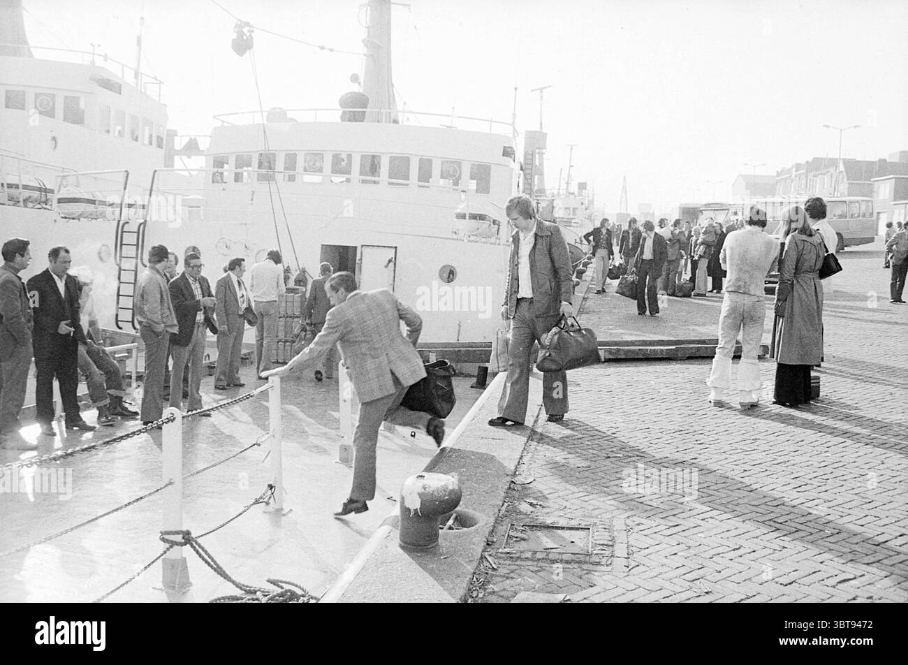 Abreise der Heringsflotte von IJmuiden Fisheries und anderen Fischhändlern Fishing, Whizgle News, Dutch Desk, Niederlande, 1950 - 2000 am 20.05.1975. Die Abbildung zeigt diese Themen. Die Szene entfaltet sich in einem belebten Hafen, möglicherweise an einem sonnigen Tag. Menschen sind am Pier verstreut, einige gehen aktiv an Bord, während andere sich unterhalten oder einfach die Umgebung beobachten. Die Umgebung verfügt über eine Flotte von Booten, einige groß und weiß, wobei die Sonne von ihren glatten Oberflächen reflektiert wird und einen glänzenden Pfad auf dem Wasser schafft. Das Dock besteht aus verwitterten Holzdielen, Anordnung Stockfoto