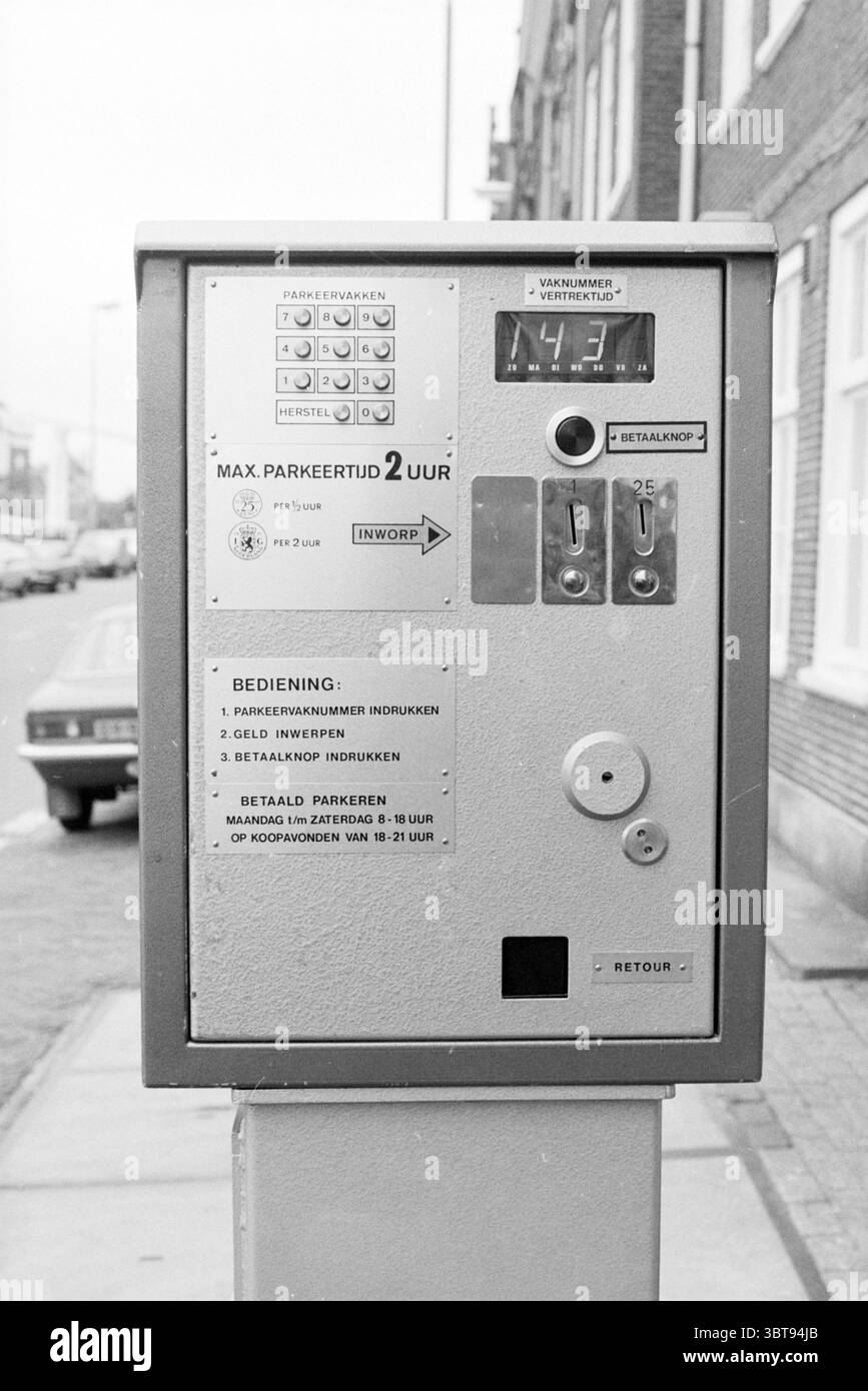 Einführung des Parkautomaten mit weiblicher Person, Whizgle News, Dutch Desk, Niederlande, 1950 - 2000 im Jahr 1981. Dies sind die Elemente im Bild. Die Szene zeigt eine Parkuhr vor dem Hintergrund einer Stadtstraße, die sich durch klare Linien und eine strukturierte Umgebung auszeichnet. Das Messgerät selbst ist metallisch und rechteckig und weist eine Kombination aus Silber- und Grautönen auf. Seine Oberfläche schimmert leicht unter dem Umgebungslicht und verleiht ihm ein leicht industrielles Gefühl. Die Vorderseite des Messgeräts ist mit verschiedenen Tasten und Schlitzen verziert, von denen einige dezent beleuchtet sind. Die Schaltflächen Stockfoto