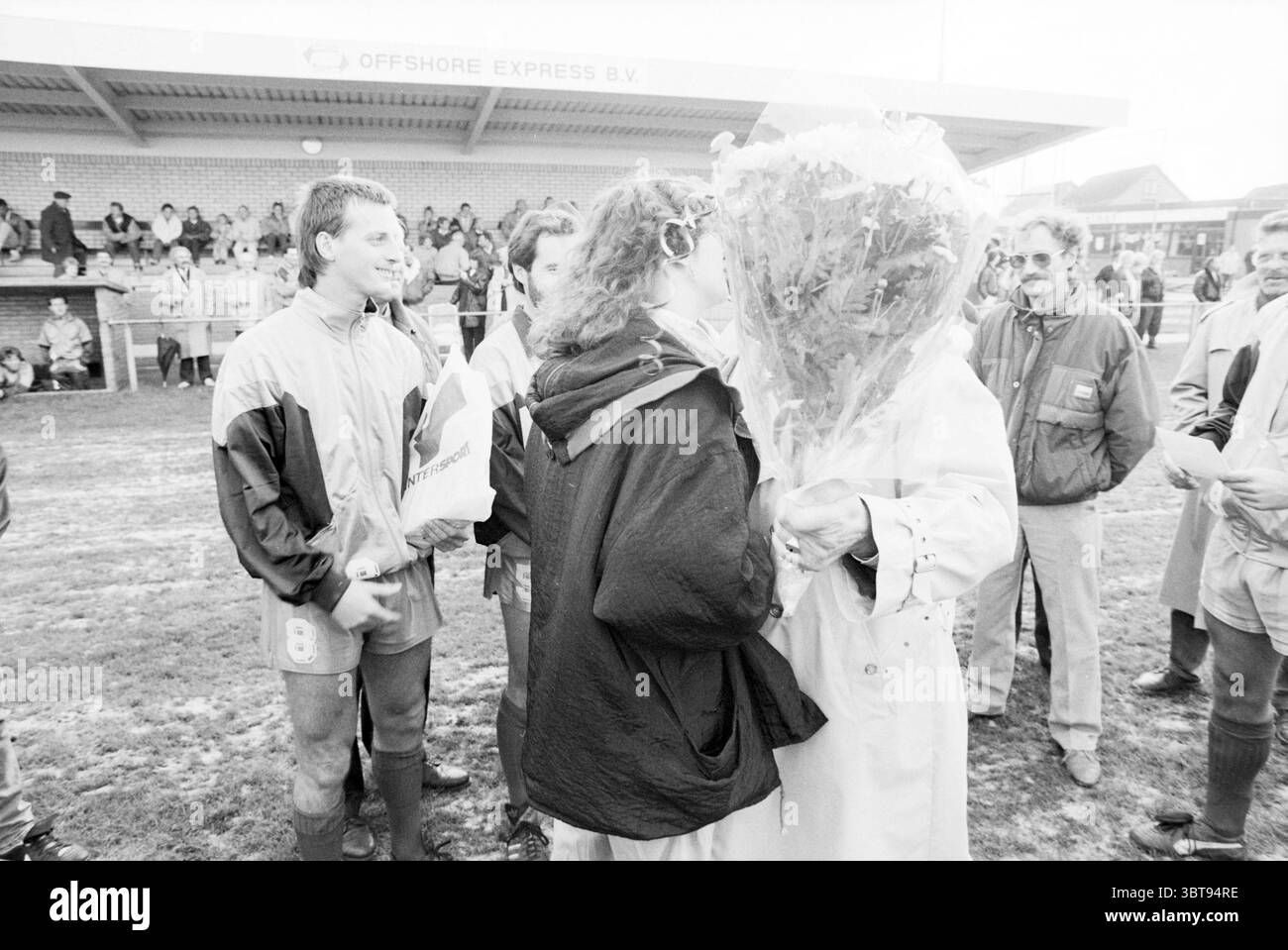 Wijk aan Zee Fußballspieler und Trainer Wijk aan Zee, Whizgle News, Dutch Desk, Niederlande, 1950 - 2000 am 05.11.1989. Diese Themen sind in der Abbildung dargestellt. Die Szene fängt einen Moment der Feier ein, wahrscheinlich nach einem Sportereignis. Im Vordergrund wird eine Gruppe von Individuen versammelt, deren fröhliche Ausdrücke das Gefühl der Leistung widerspiegeln. Eine Person, die einen großen Blumenstrauß erhält, ist fast von den Blüten umgeben, die reichlich vorhanden sind und möglicherweise eine Mischung aus lebhaften Farben sind, obwohl die monochromen Töne die Sichtbarkeit von Farbtönen einschränken. Der Empfänger der Blumen Stockfoto